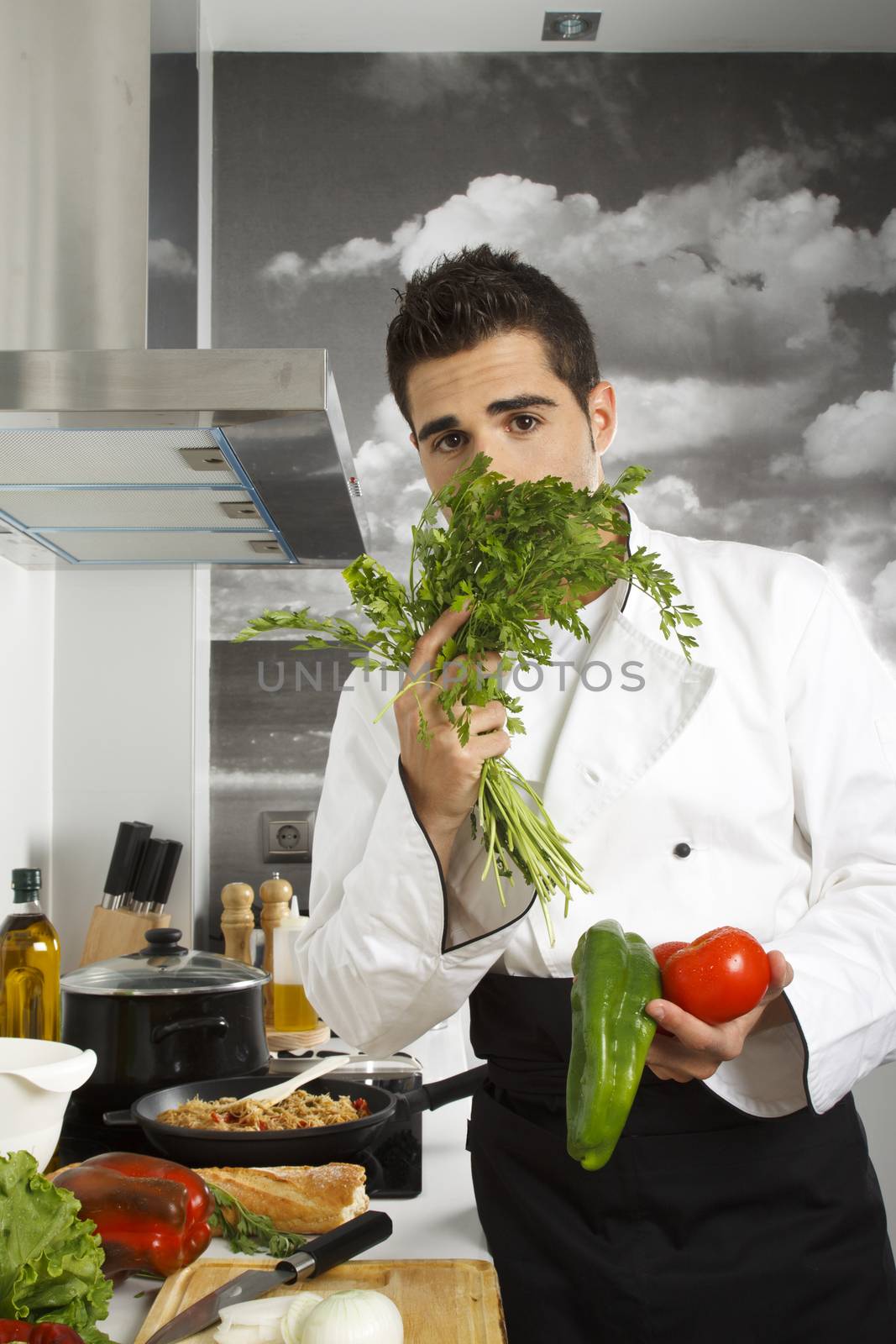 Chef smelling parsley and he has vegetables in other hand.