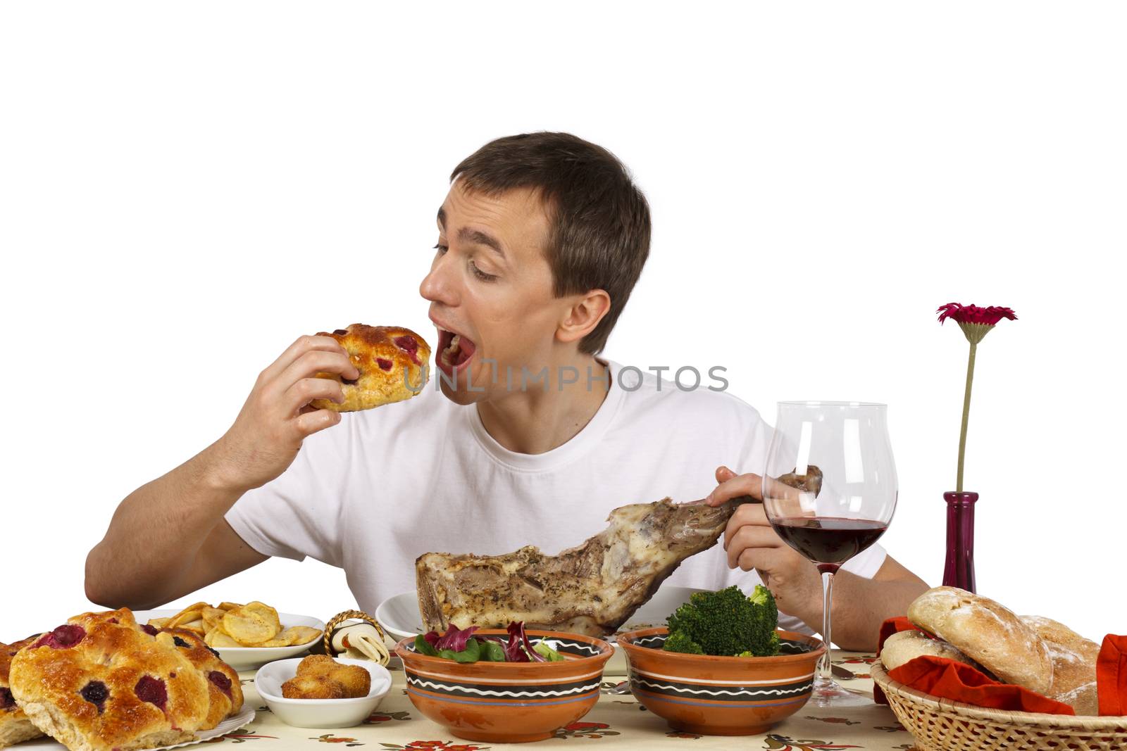 Young man eating a cake while he holds a leg of lamb. Isolated of white background.