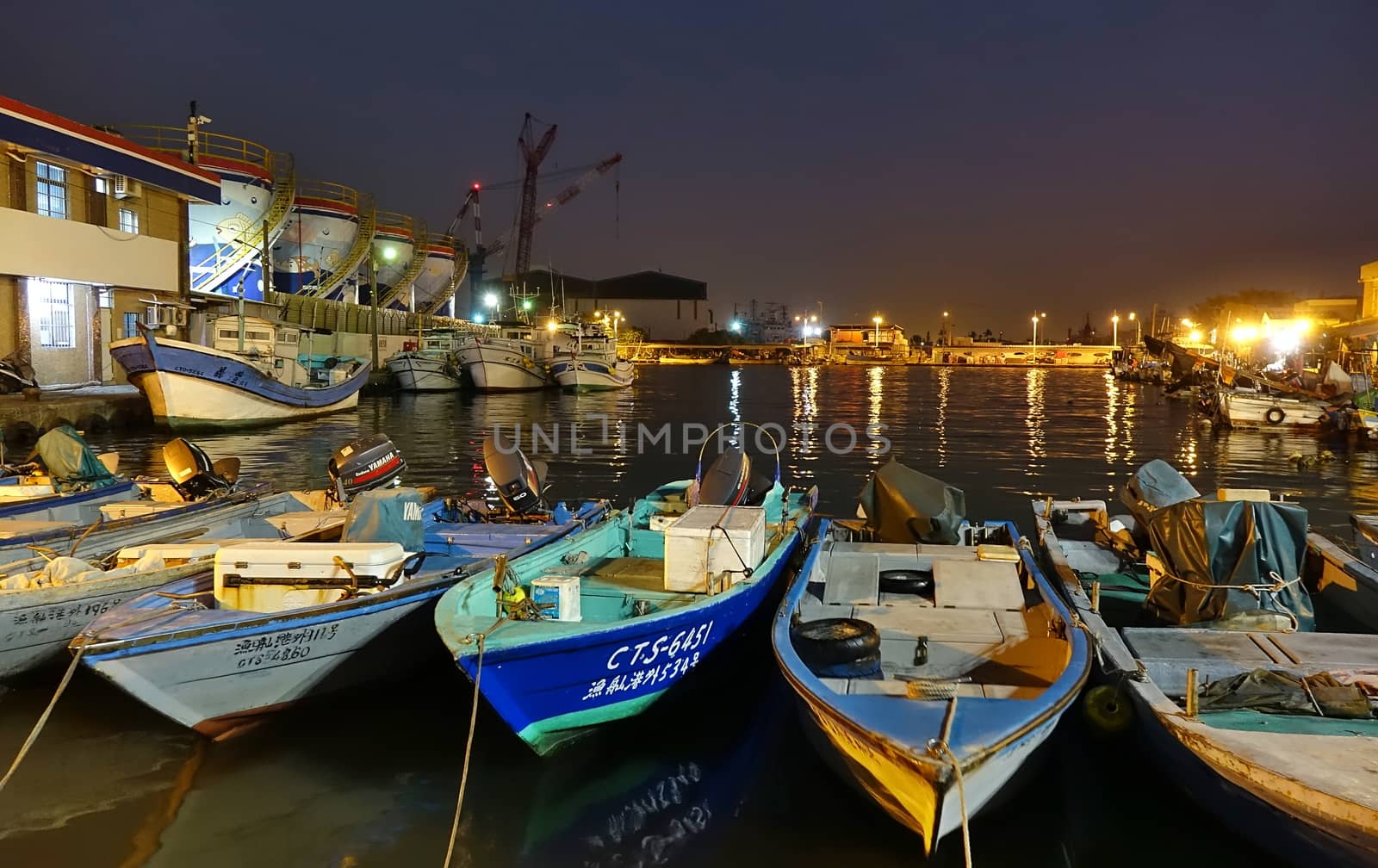 KAOHSIUNG, TAIWAN -- DECEMBER 22, 2018: A small fishing harbor by night on the island of Qijin. In the back are colorful fuel storage tanks.
