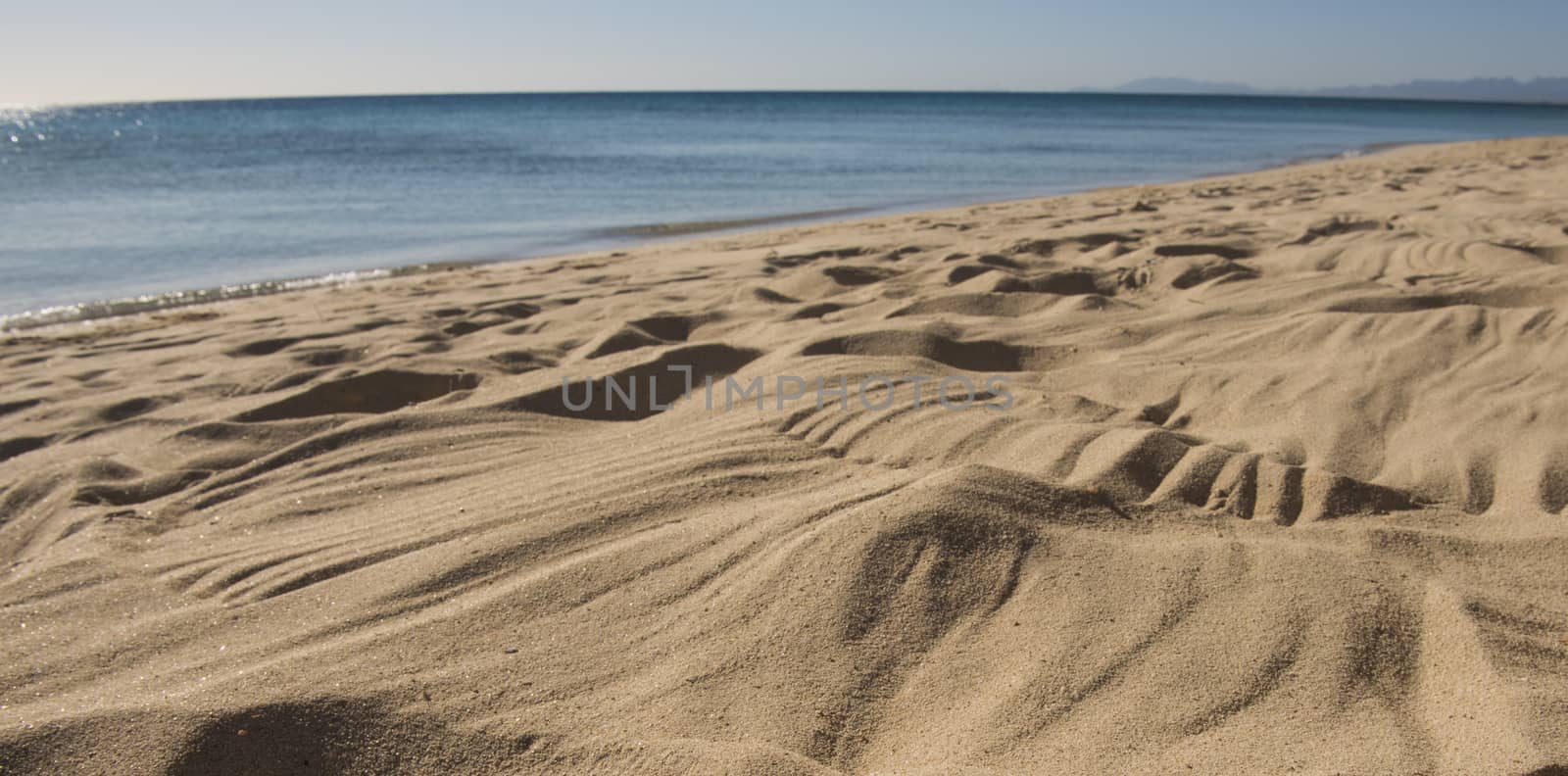 Closeup view across an empty sandy tropical beach to the open ocean with horizon in distance