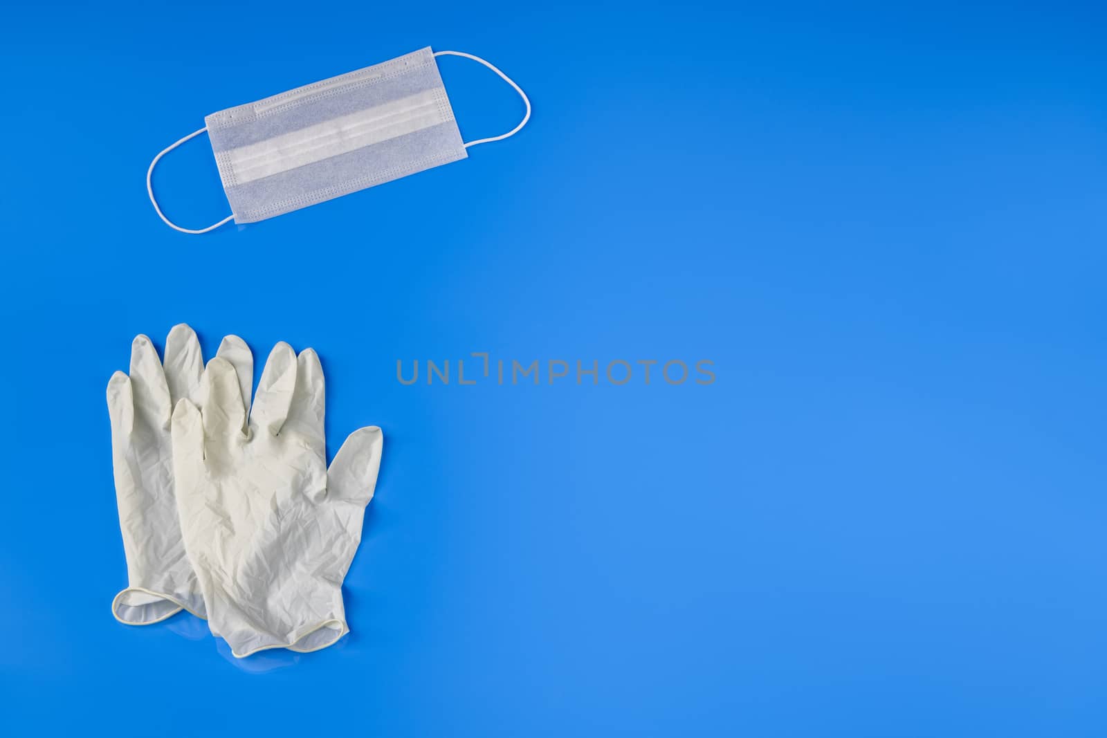 Personal Protective Equipment (PPE) kit against coronavirus with face mask, set of gloves against blue background with copy space for title or text.
