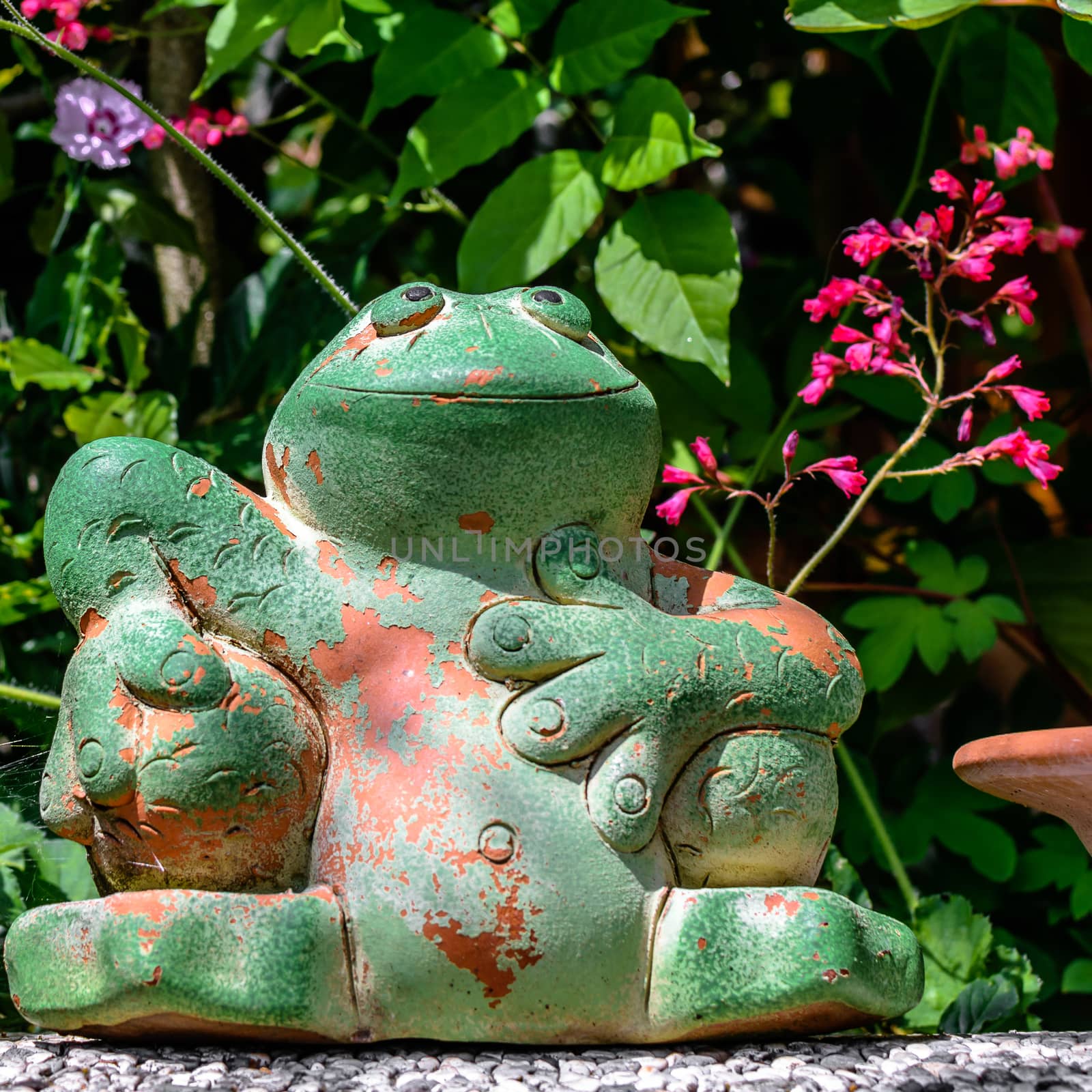 Pretty green potted frog sitting on a wall in front of flowers by Umtsga