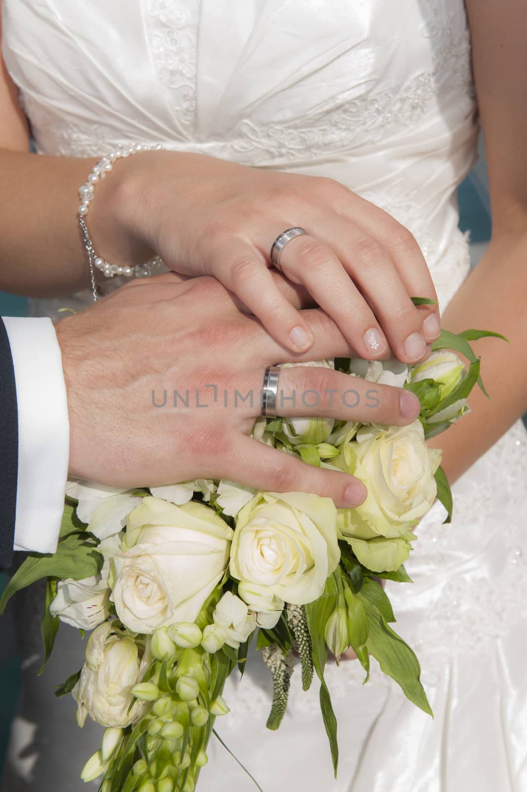 Hands of a bride and groom at a wedding ceremony showing a bouquet and rings