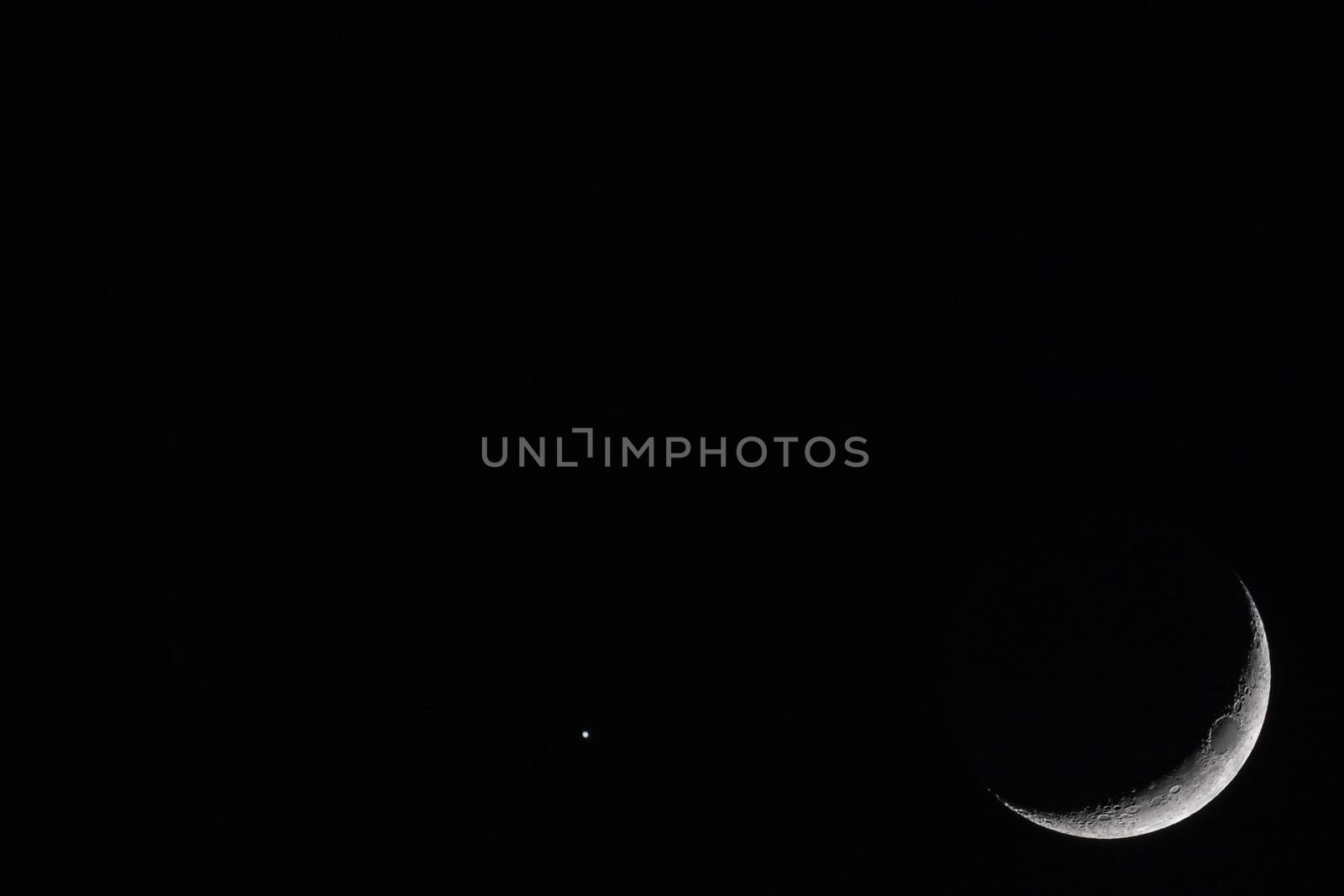 Crescent Moon with bright star against black sky at night with large copy space