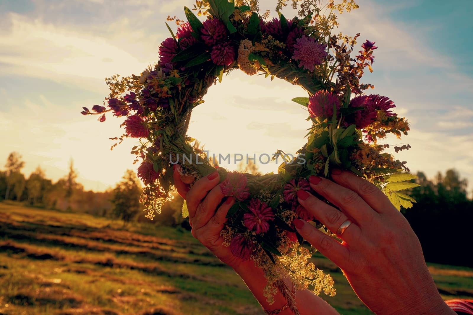 Hands with a wreath of Midsummer flowers against the sunset