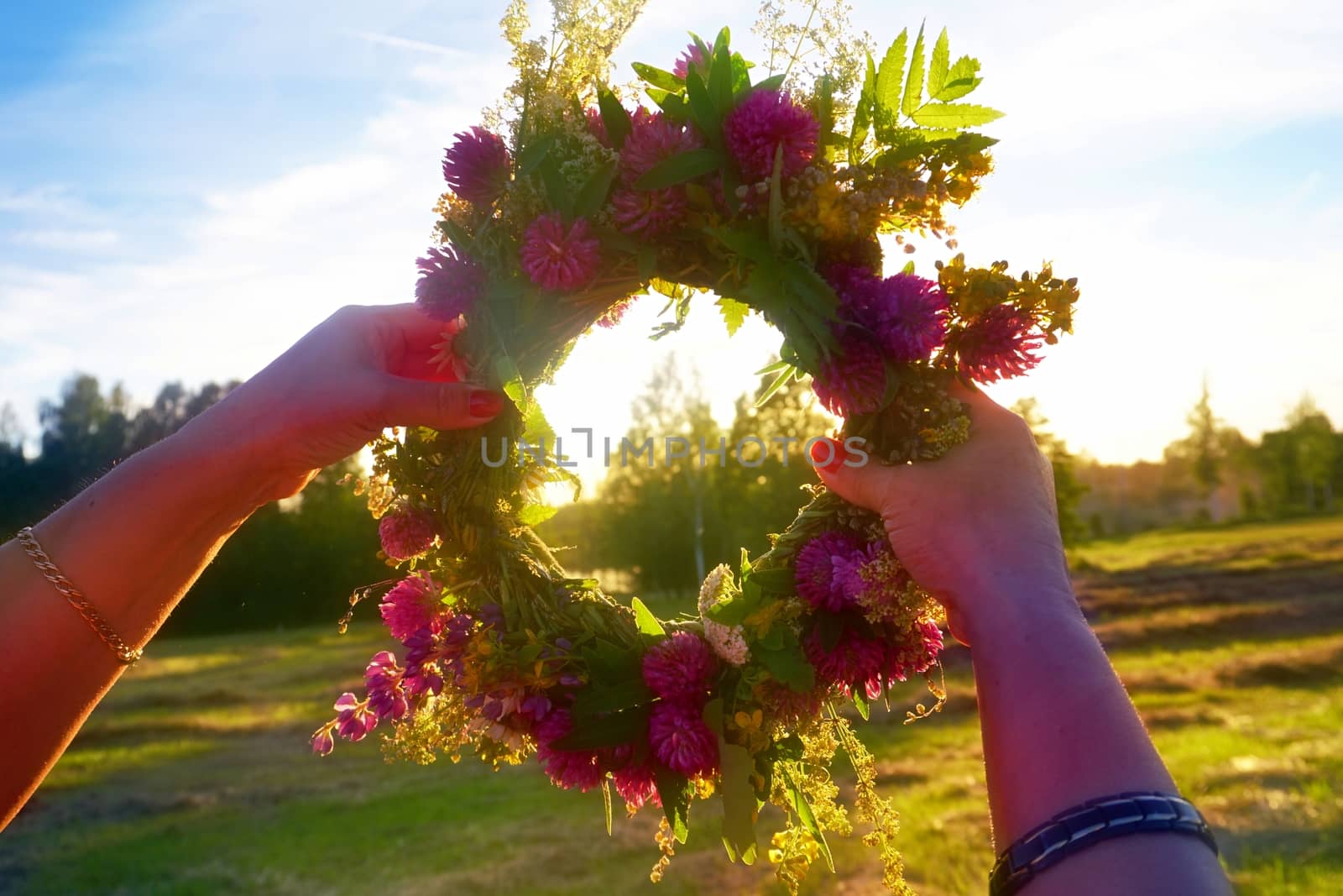 Hands with a wreath of Midsummer flowers against the sunset