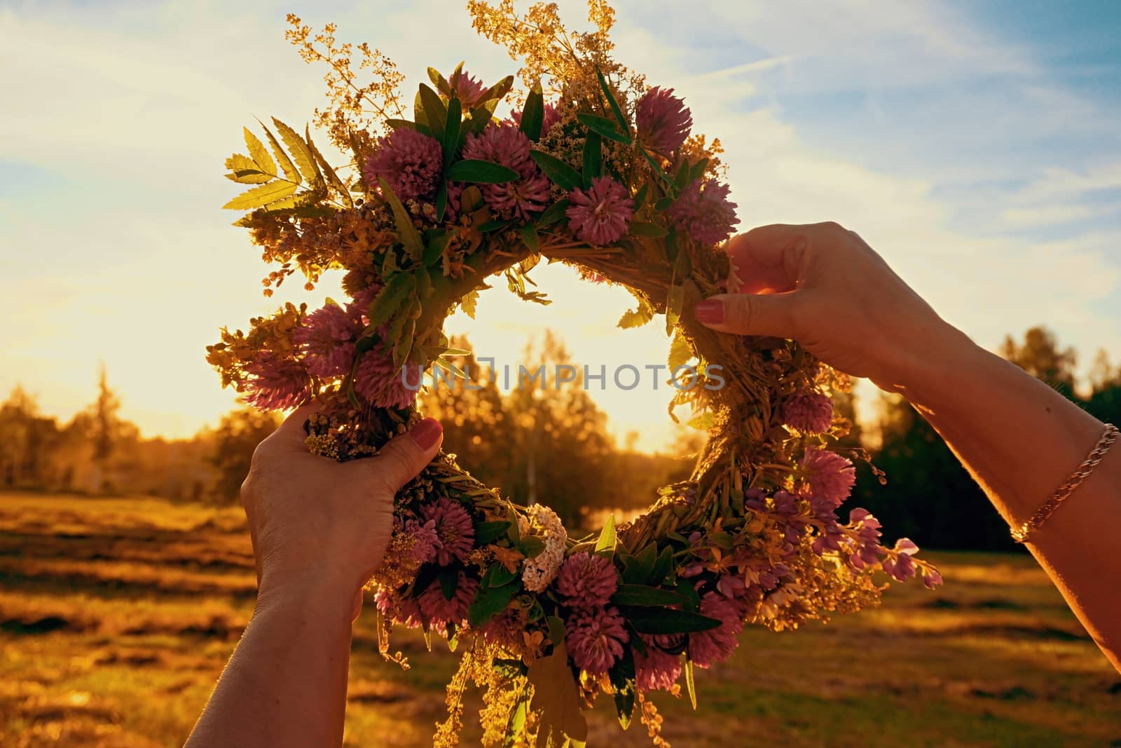 Hands with a wreath of Midsummer flowers against the sunset