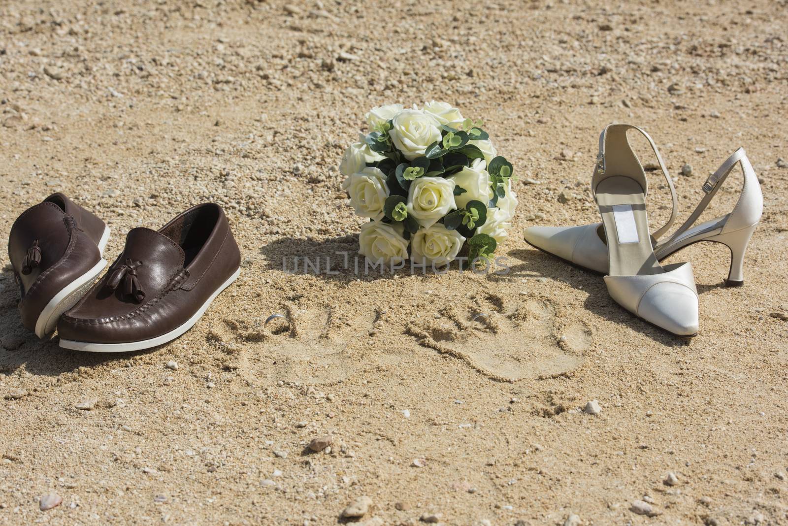 Bride and grooms shoes and handprints on beach in sand with wedding rings and bouquet