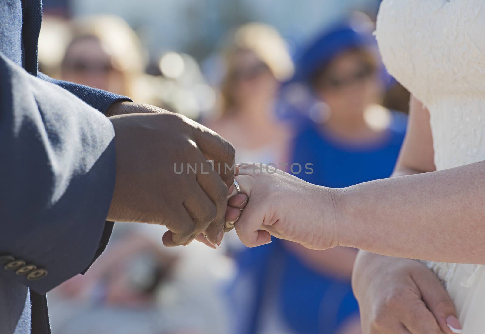 Groom placing a ring on brides finger at wedding ceremony with mixed race couple