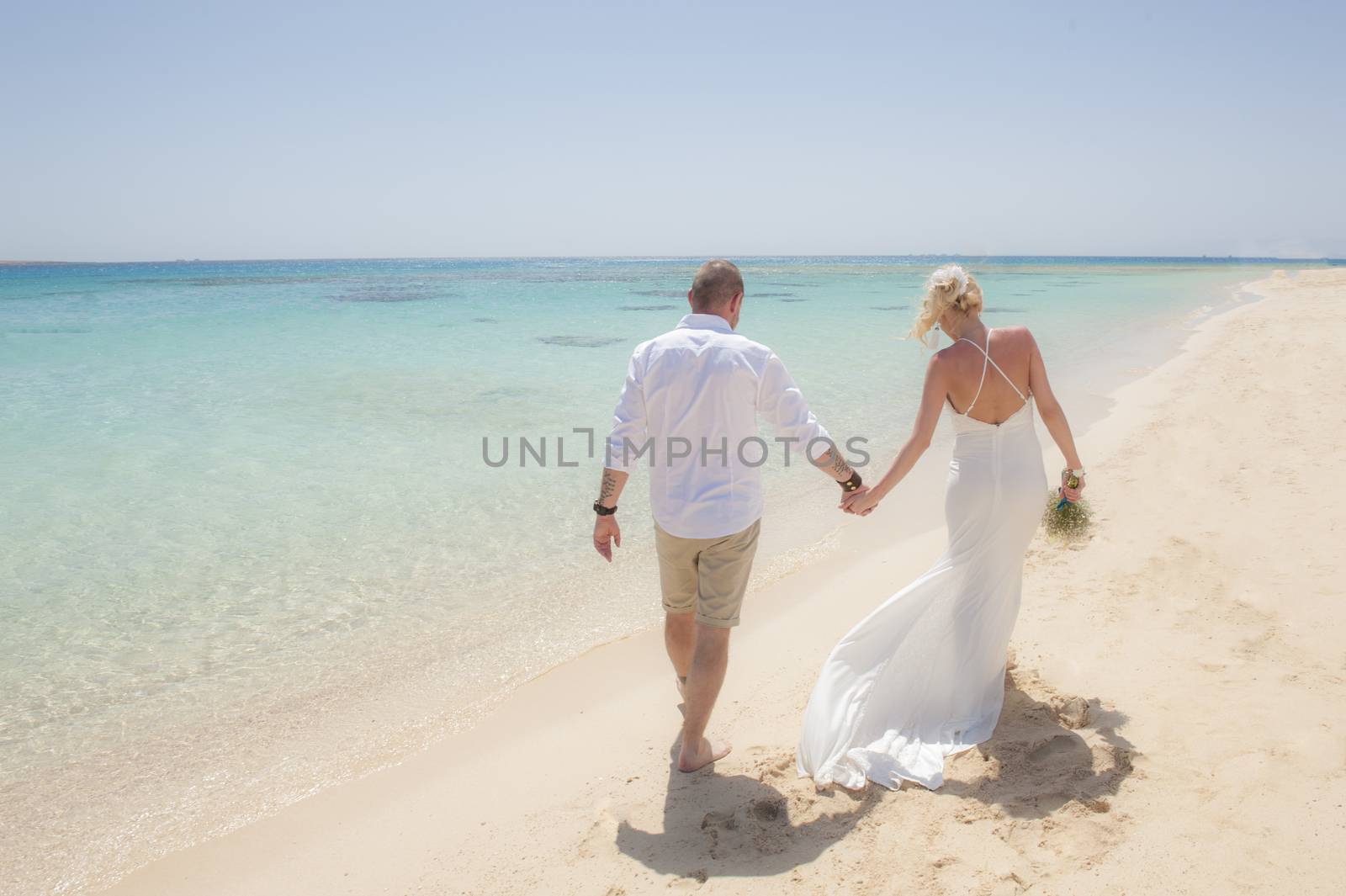 Beautiful couple walking together at a tropical beach paradise on wedding day in white gown dress with ocean view