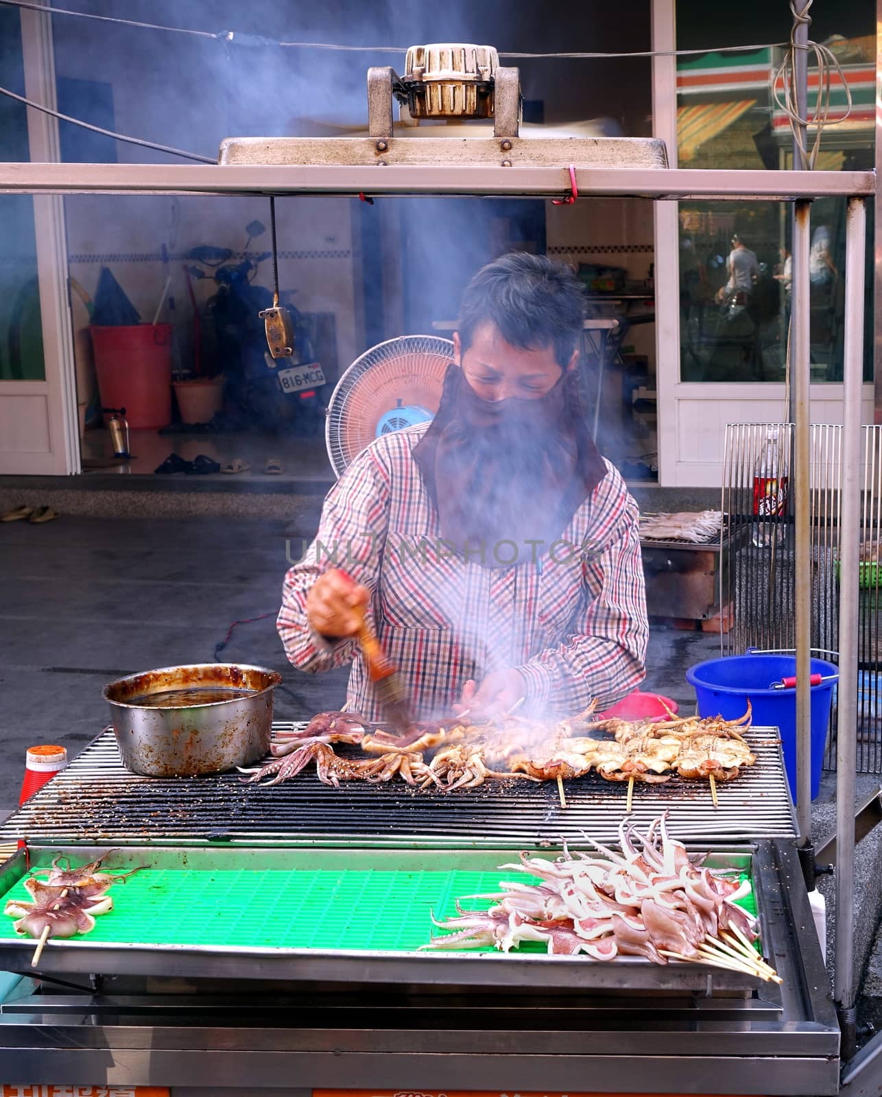 KAOHSIUNG, TAIWAN -- OCTOBER 11, 2014: An outdoor vendor applies barbeque sauce on fresh squid on a charcoal grill.