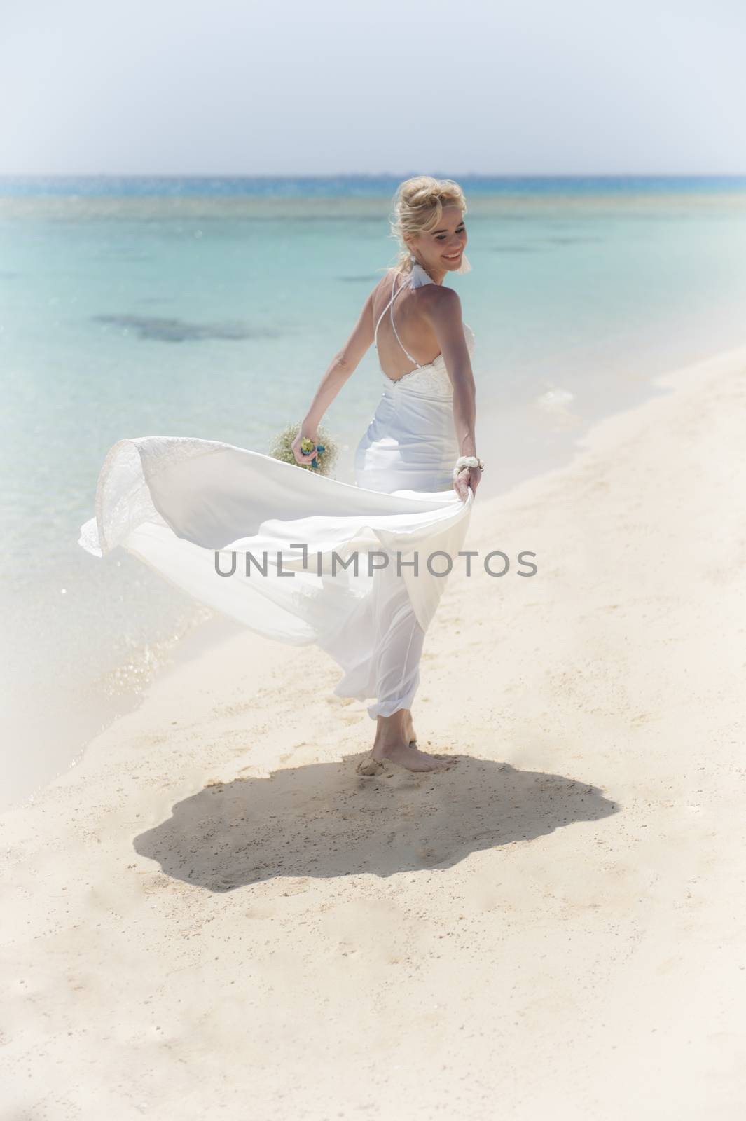 Beautiful woman bride at a tropical beach paradise on wedding day in flowing white gown dress with ocean view