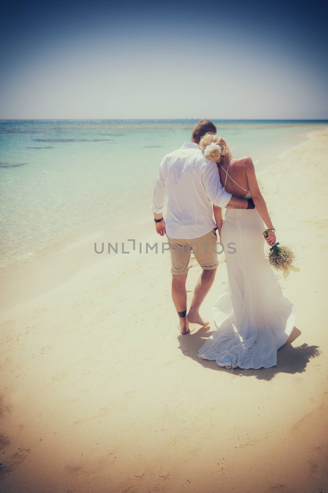 Beautiful couple holding each other at a tropical beach paradise on wedding day in white gown dress with ocean view vintage style photo