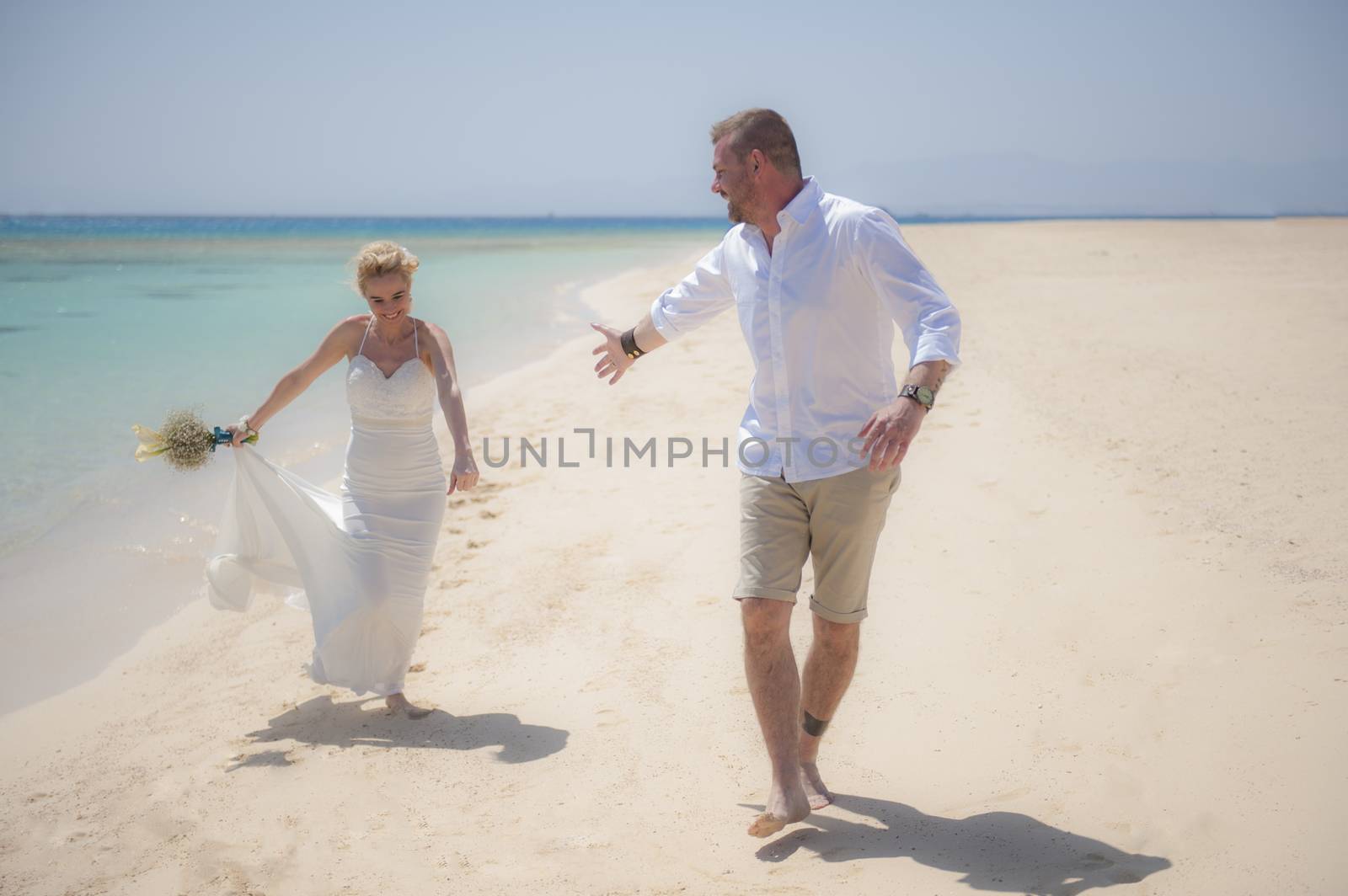 Beautiful couple walking together at a tropical beach paradise on wedding day in white gown dress with ocean view