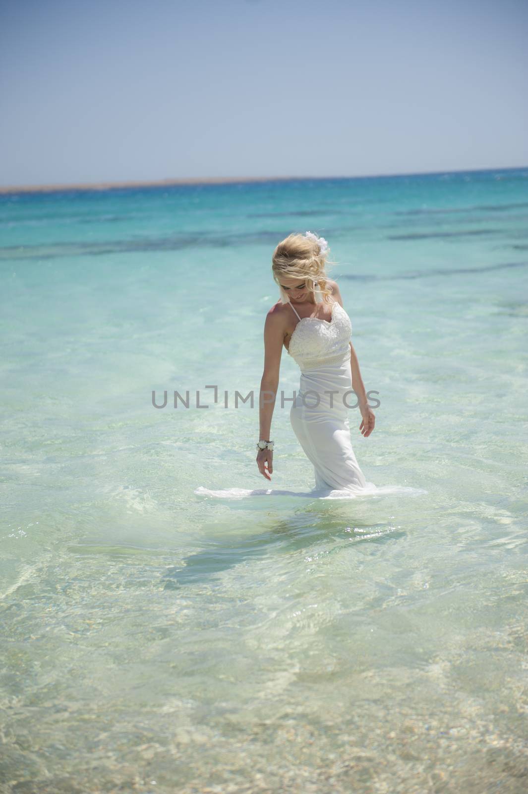 Beautiful woman bride at a tropical beach paradise on wedding day in white gown dress with ocean view walking through water