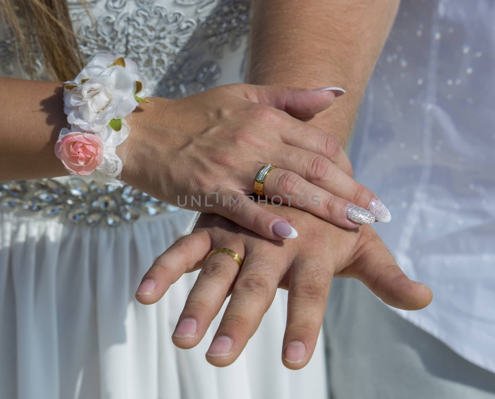Closeup detail of bride and groom hands on wedding day with rings and bouquet flowers