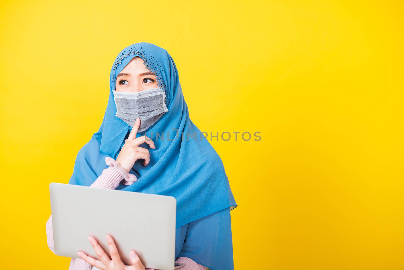 Asian Muslim Arab, Portrait of happy beautiful young woman Islam religious wear veil hijab and face mask protect she quarantines disease coronavirus hold laptop computer and thinking question