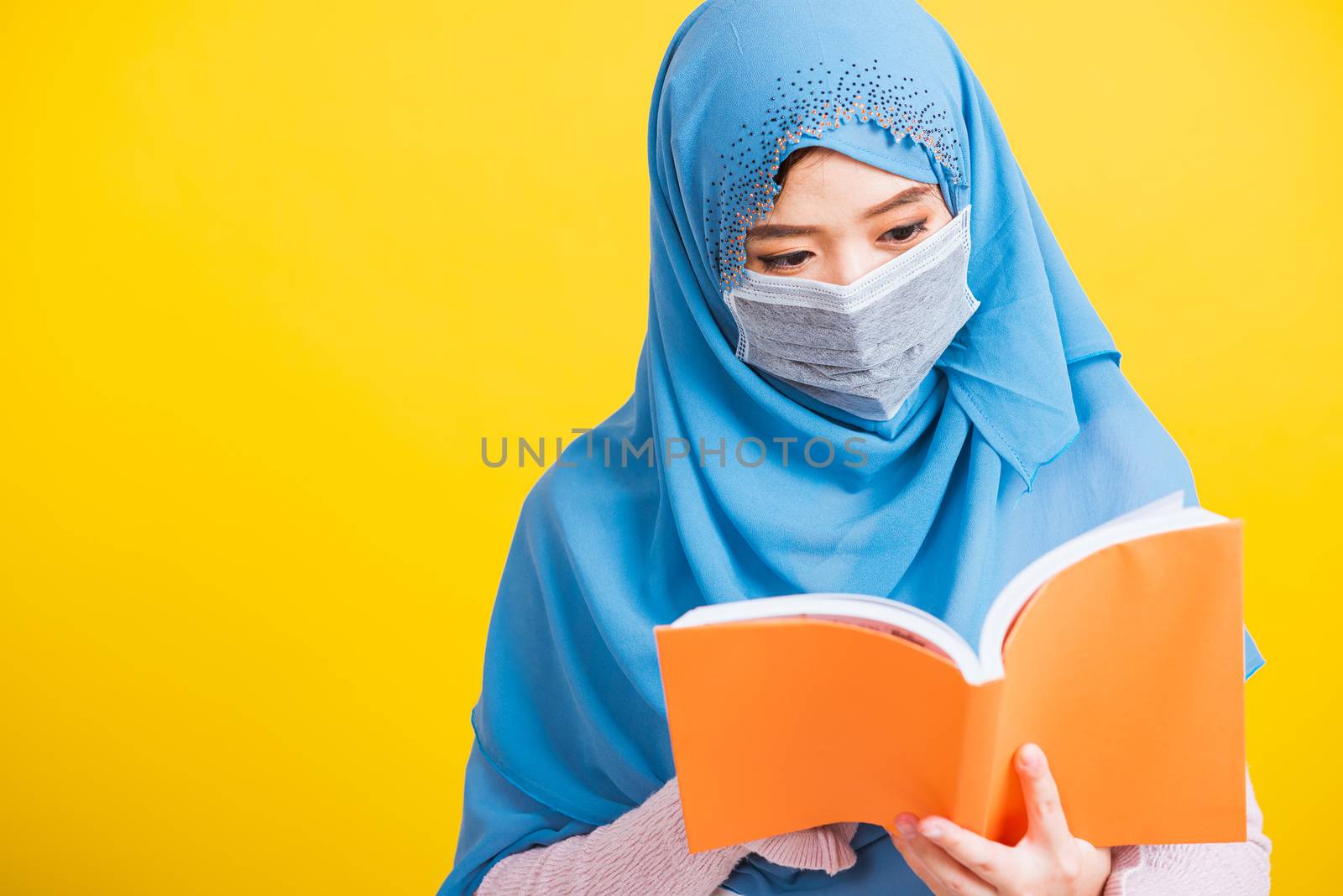 Asian Muslim Arab, Portrait of happy beautiful young woman religious wear veil hijab and face mask protective to prevent coronavirus she hold book on hand and open reding it on yellow, Back to college