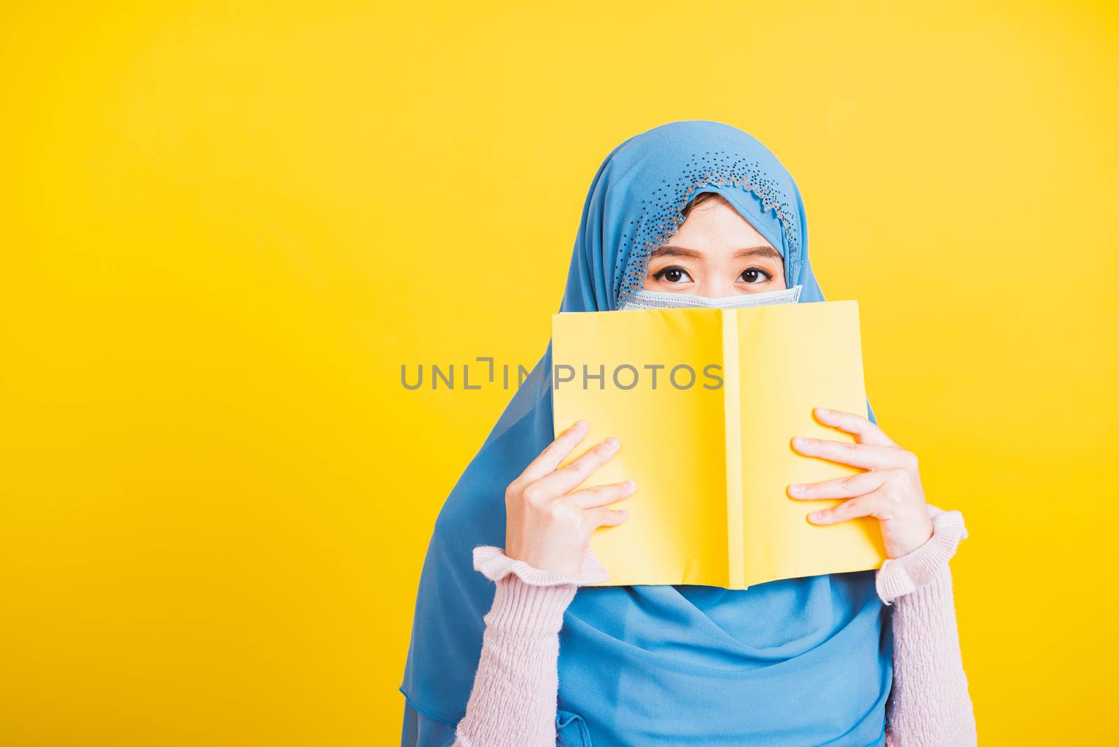 Asian Muslim Arab, Happy beautiful young woman religious wear veil hijab and face mask to prevent coronavirus she student hold books close face, isolated on yellow background, Back to college