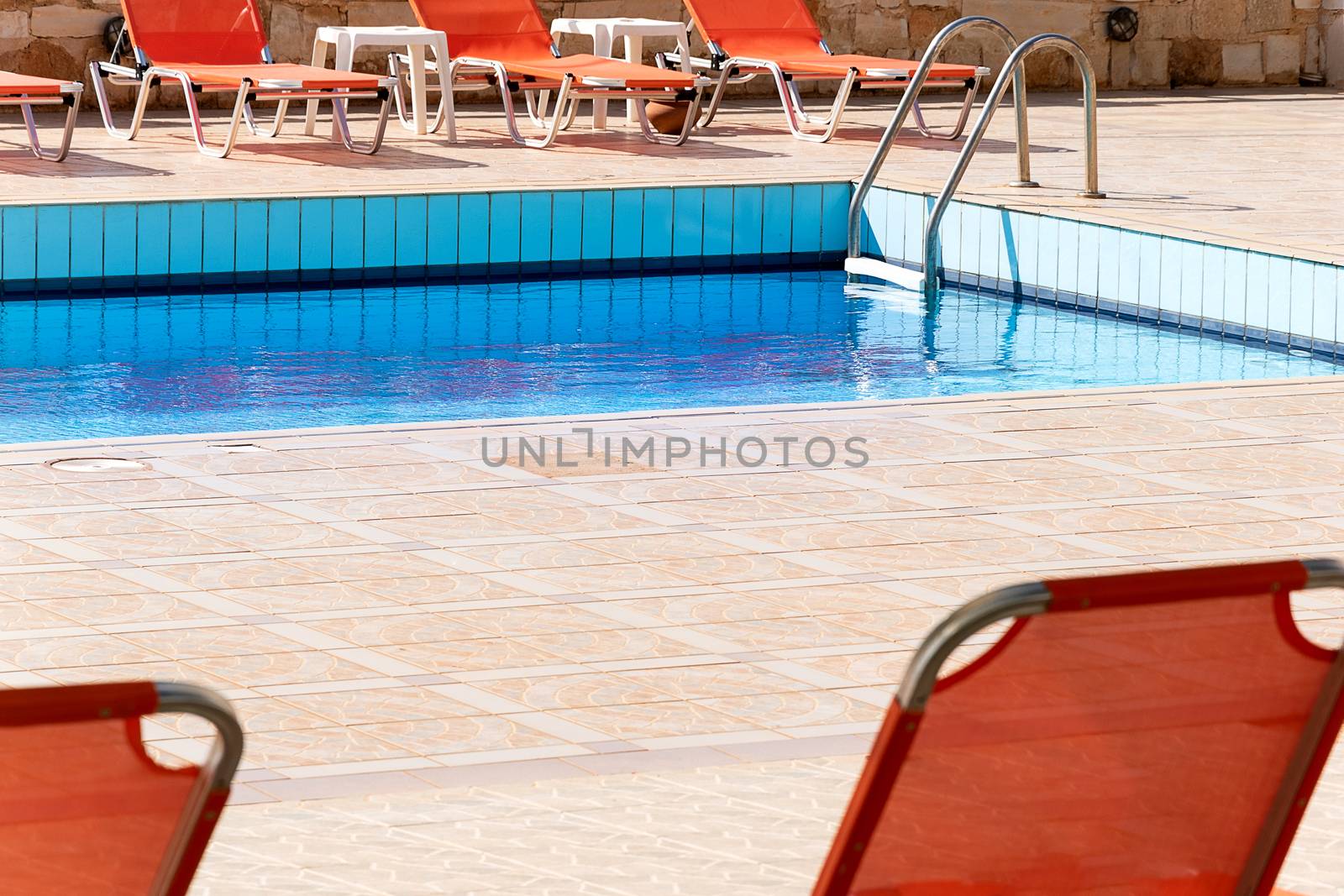 Swimming pool with empty sunbeds outside of vacation hotel. contemporary relax blue water pool  photography.  poolside with ladder and beach chairs in summertime. no people relax resort exterior.