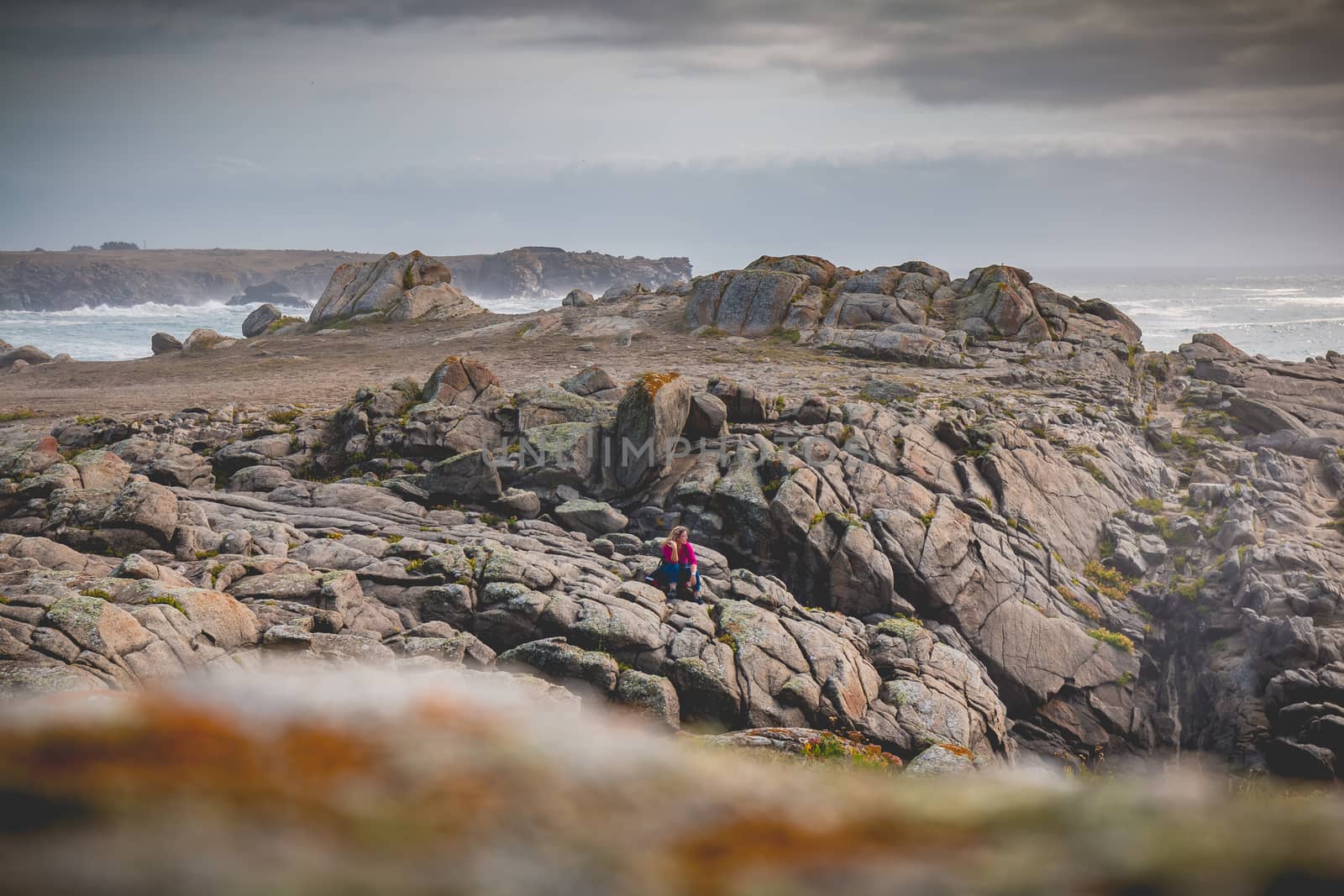 young woman sitting on rocks  of the island of Yeu by AtlanticEUROSTOXX