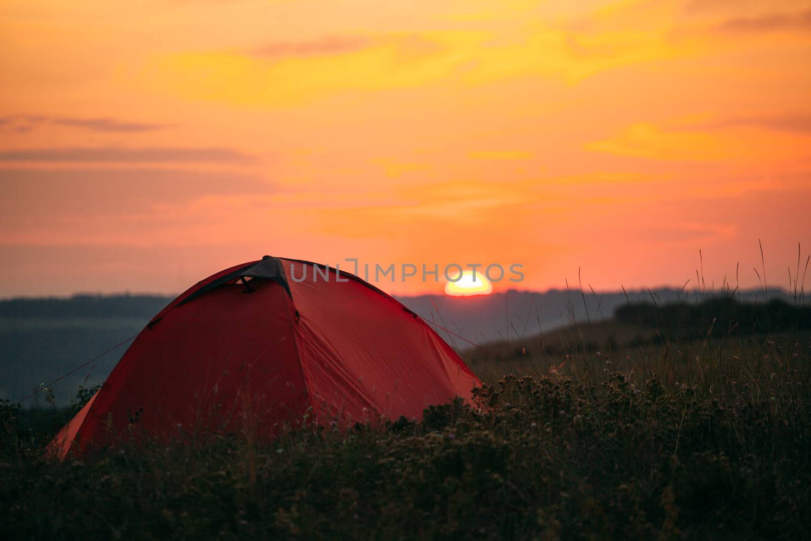 Orange tent at sunset in the mountains. Camping in nature.