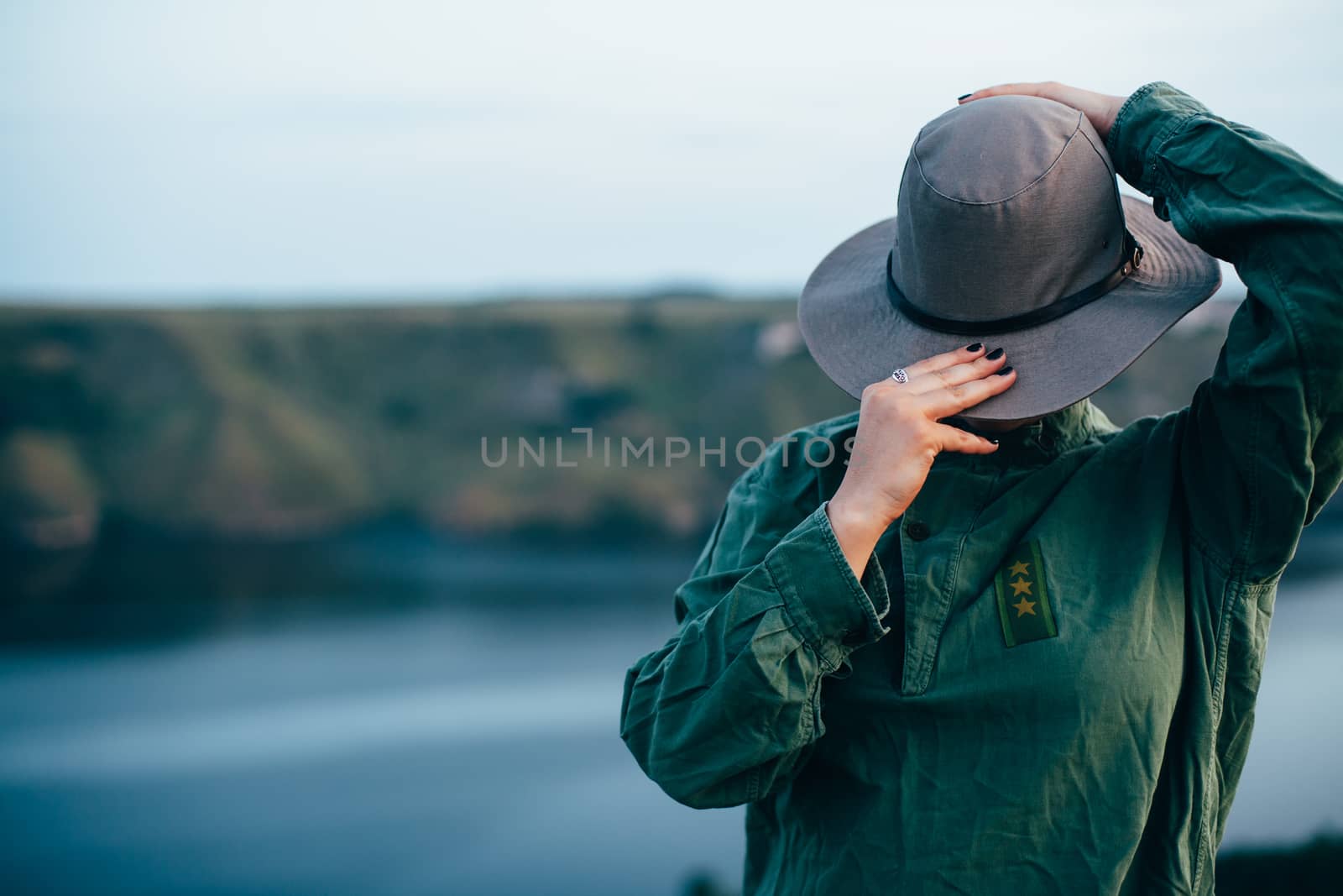 A girl stands on top of a mountain against the backdrop of a large canyon with a river. Portrait of a girl in a big hat covering her face.