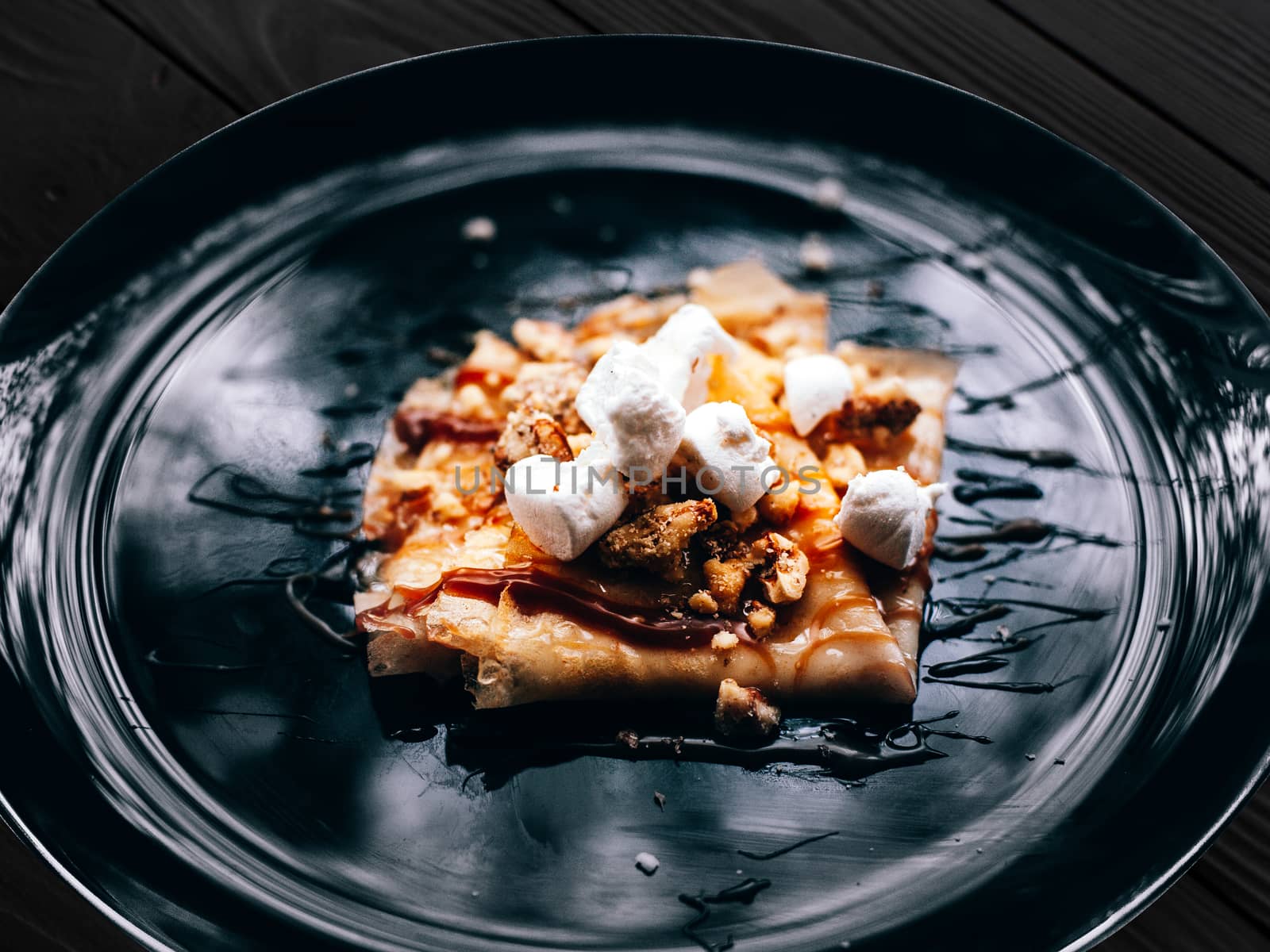 Plate with folded pancake caramel coated walnuts and marshmallow by Opikanets