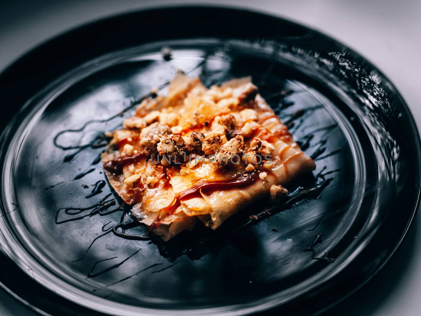 Pancakes on a black plate covered with caramel and walnuts
 by Opikanets