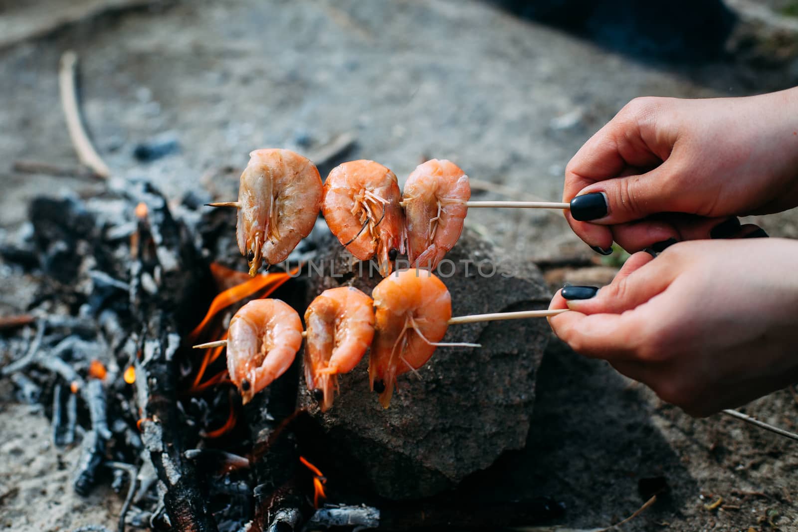 Girl holding shrimp over a bonfire. Grilled shrimp on charcoal. Food in the nature. Picnic