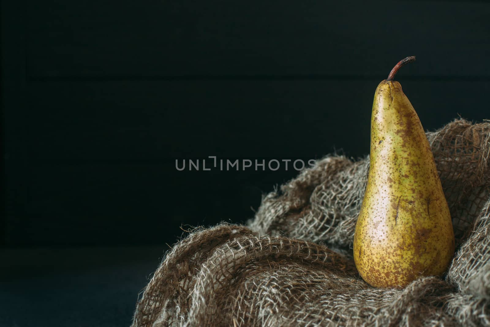 Still life with a pear standing on burlap on a dark wooden backg by Opikanets