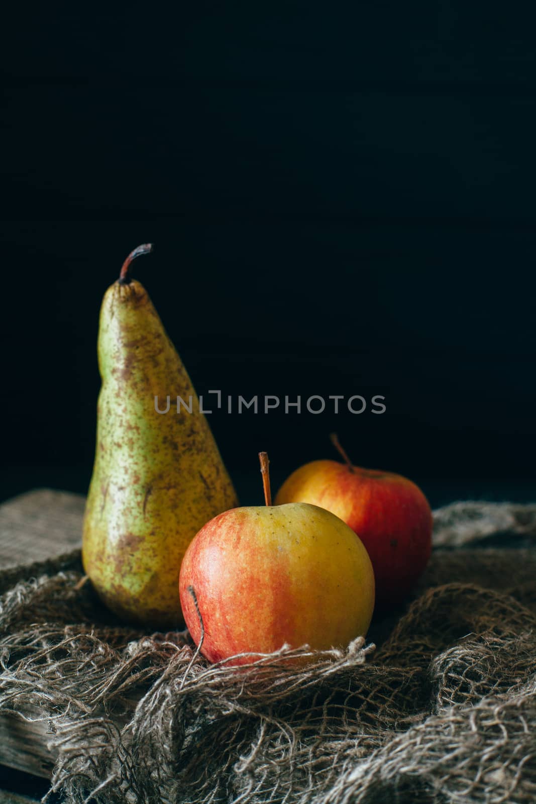 Still life with pears and apple on burlap on a dark wooden background.