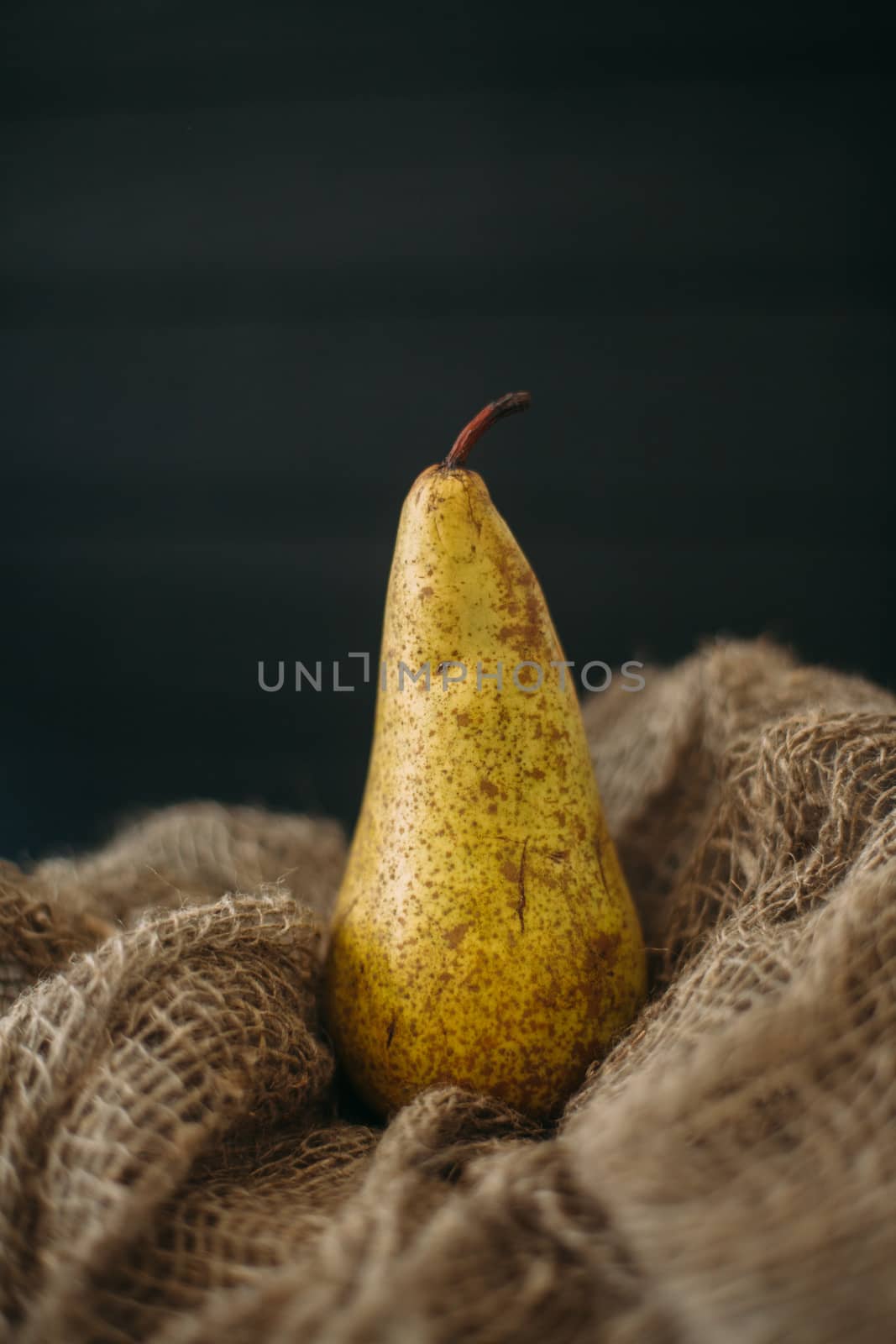 Still life with a pear standing on burlap on a dark wooden backg by Opikanets