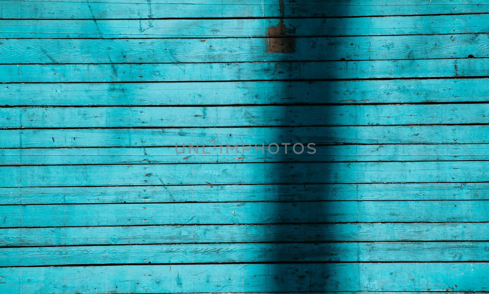 Blue wooden boards in the sunlight with a shadow from the tree. Texture of painted wood.