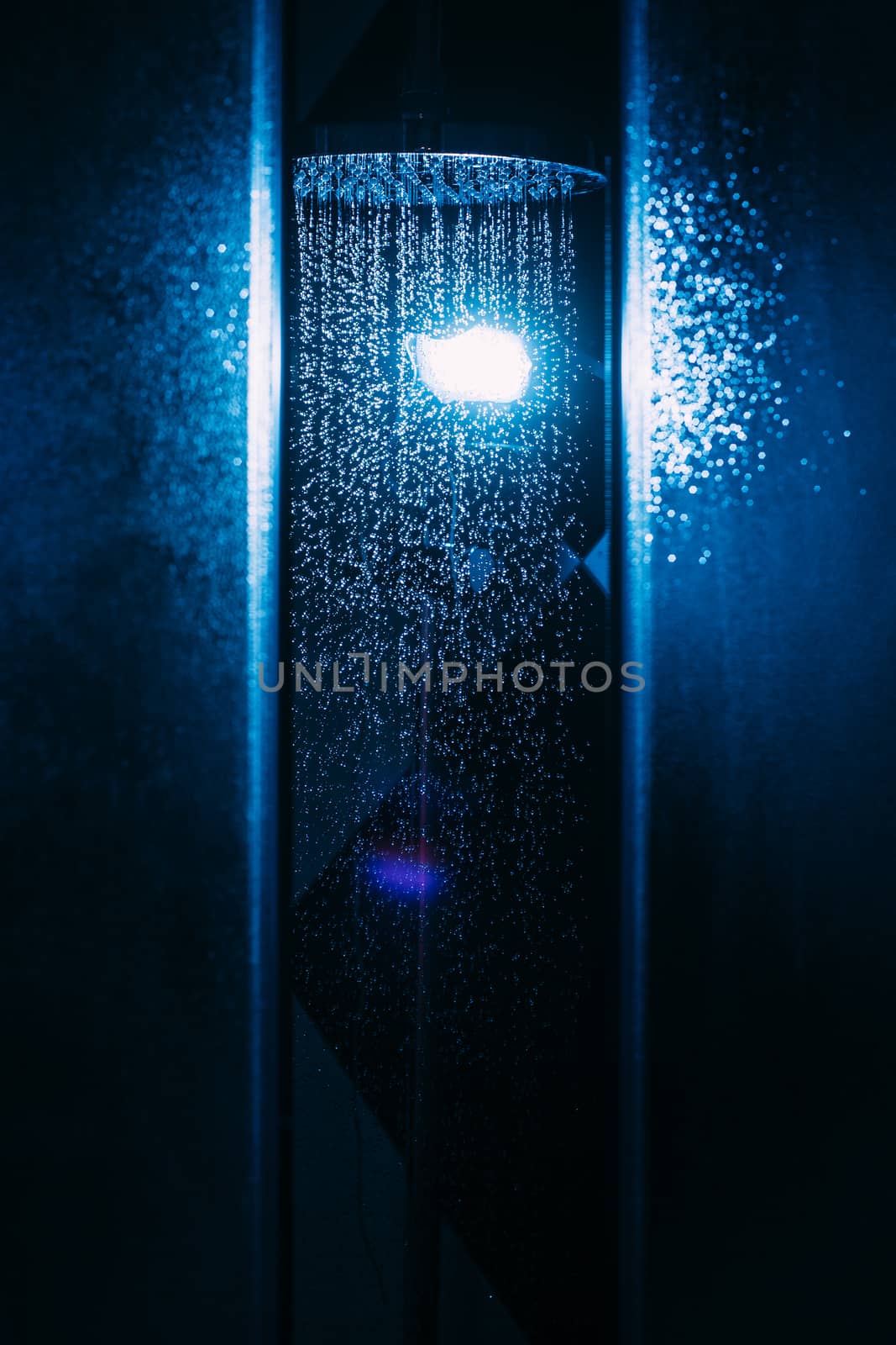 Drops of water fall from a watering can in the shower in blue light. Water drops close-up. Flow of water. A large round watering can in the shower.