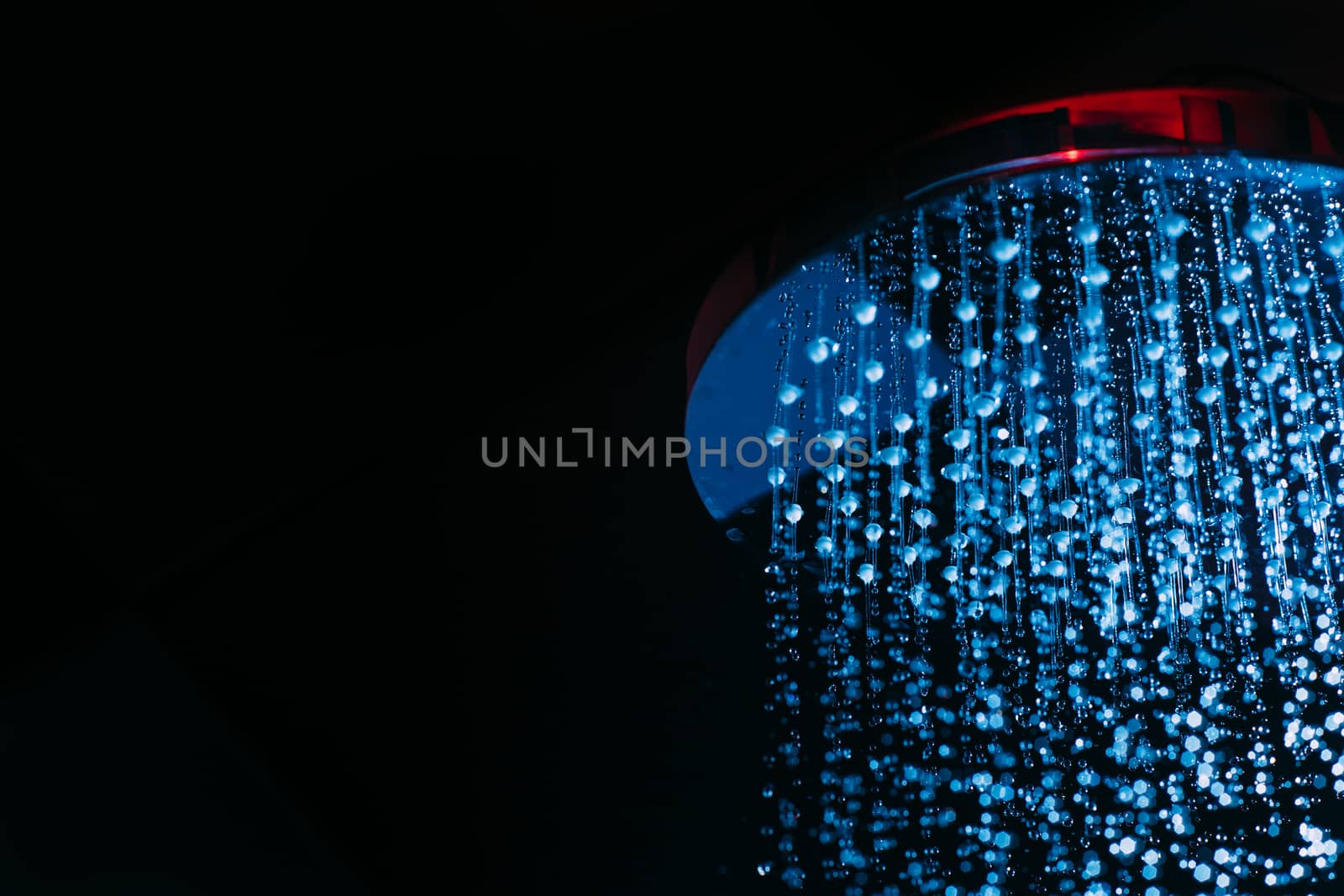 Drops of water fall from a watering can in the shower in blue light. Water drops close-up. Flow of water. Big round watering can macro photo.