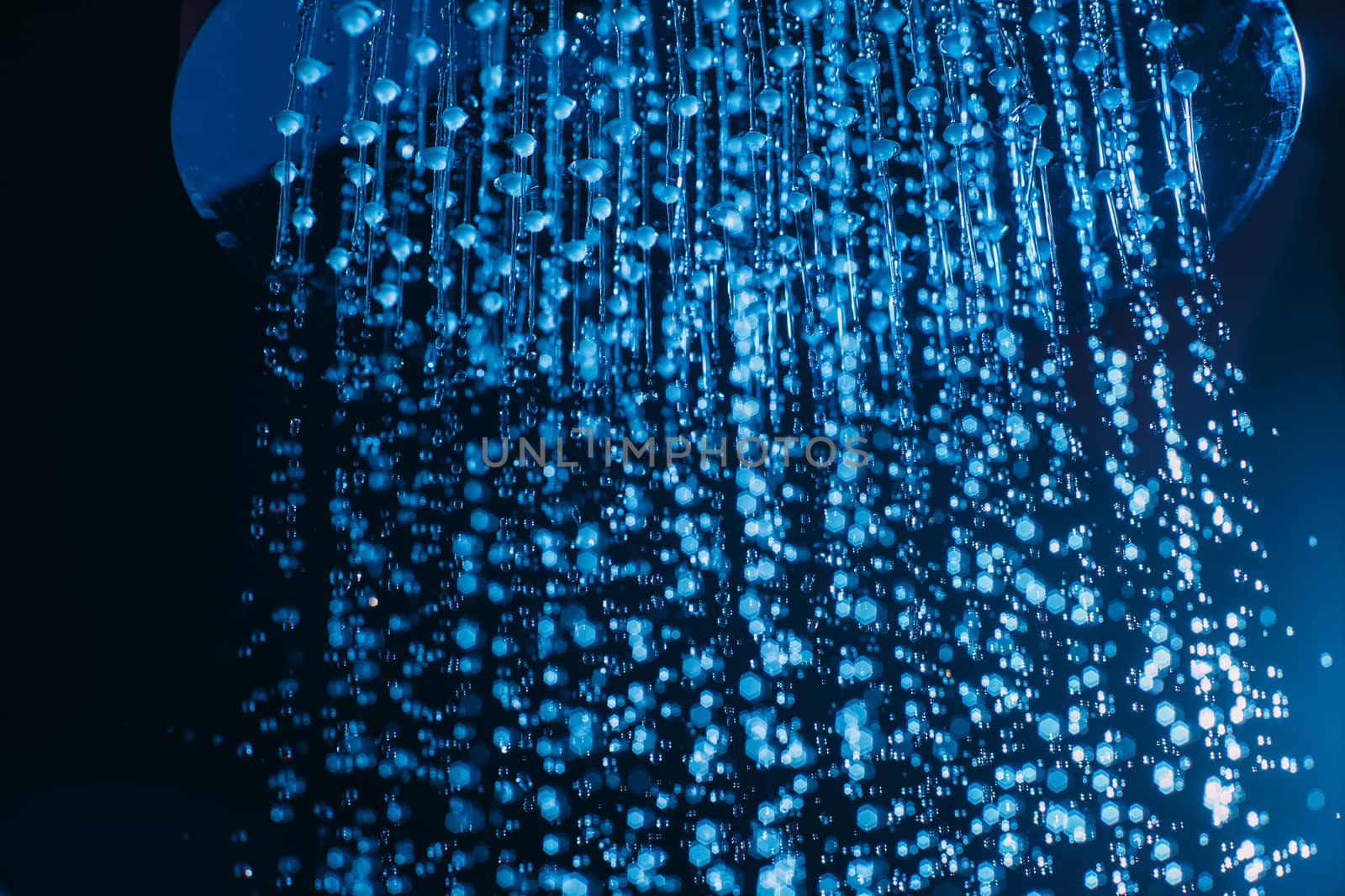 Drops of water fall from a watering can in the shower in blue light. Water drops close-up. Flow of water. Big round watering can macro photo.