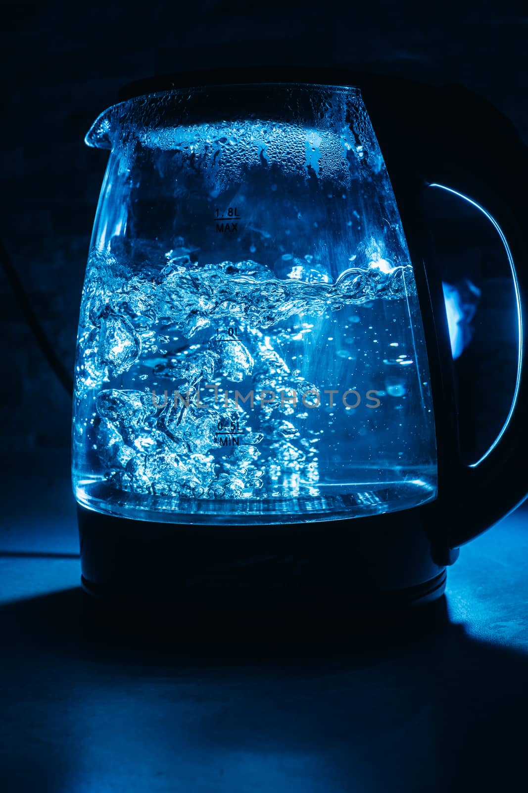 Boiling glass black teapot with blue backlight on a black background. Boiling water. Hot water is seething. Bubbles of air in the water.