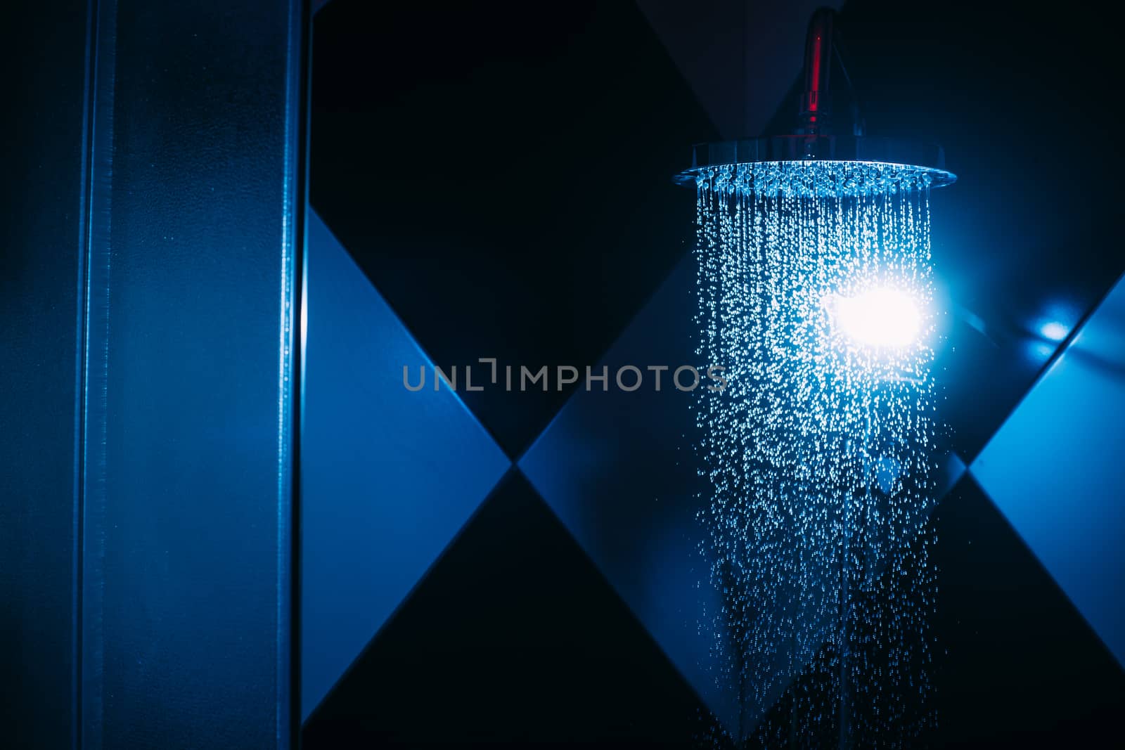 Drops of water fall from a watering can in the shower in blue light. Water drops close-up. Flow of water. A large round watering can in the shower.