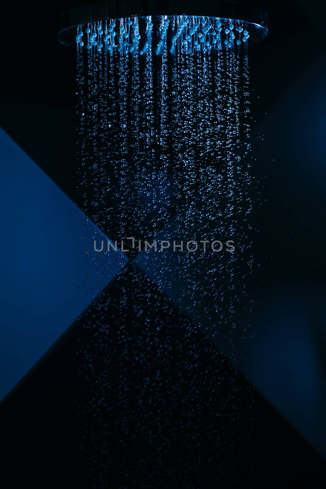 Drops of water fall from a watering can in the shower in blue light. Water drops close-up. Flow of water. A large round watering can in the shower.