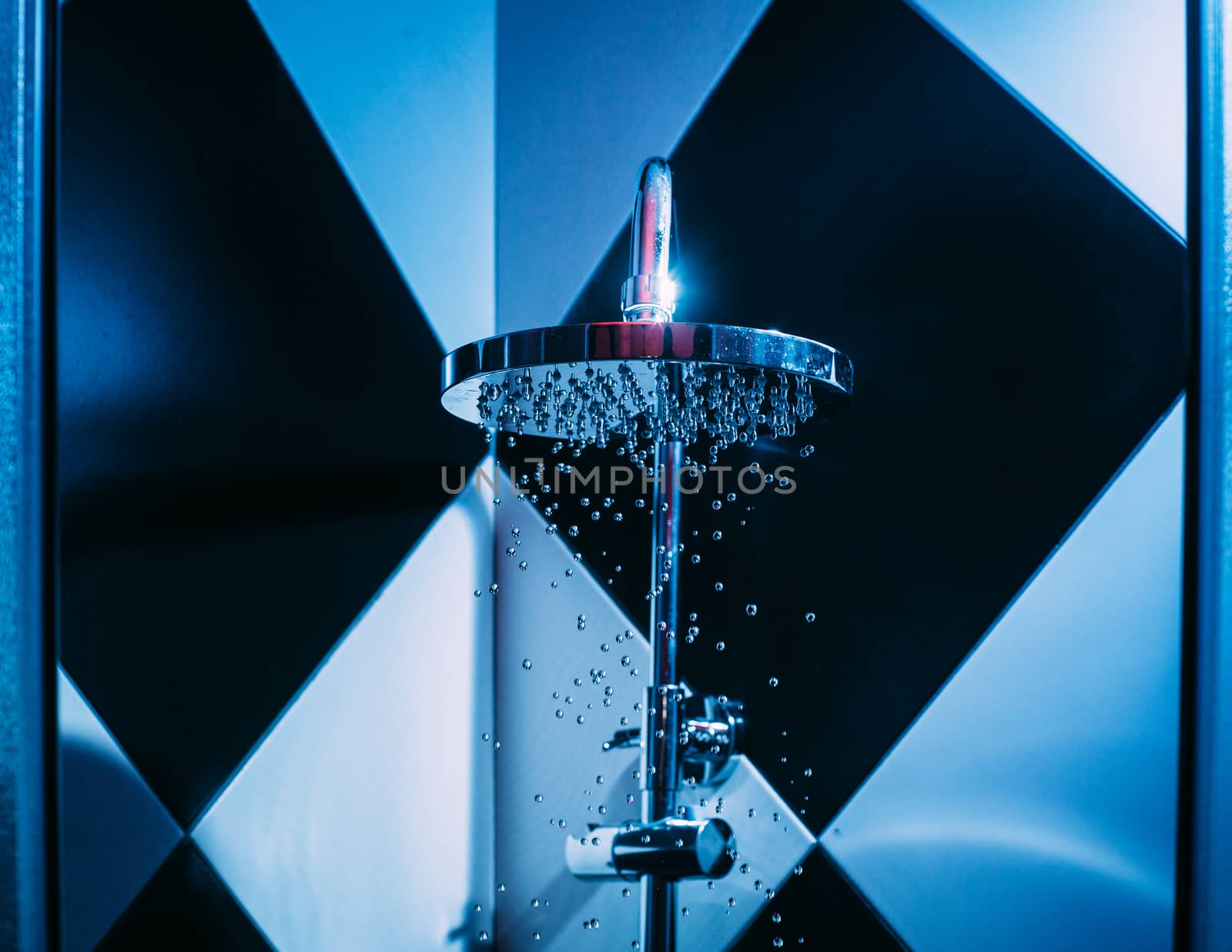 Drops of water fall from a watering can in the shower in blue light. Water drops close-up. Flow of water. A large round watering can in the shower.