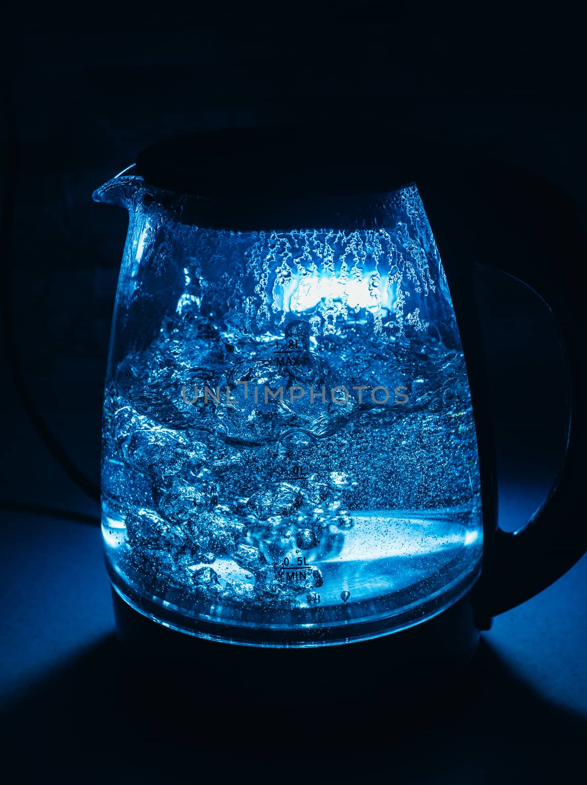 Boiling glass black teapot with blue backlight on a black background. Boiling water. Hot water is seething. Bubbles of air in the water.