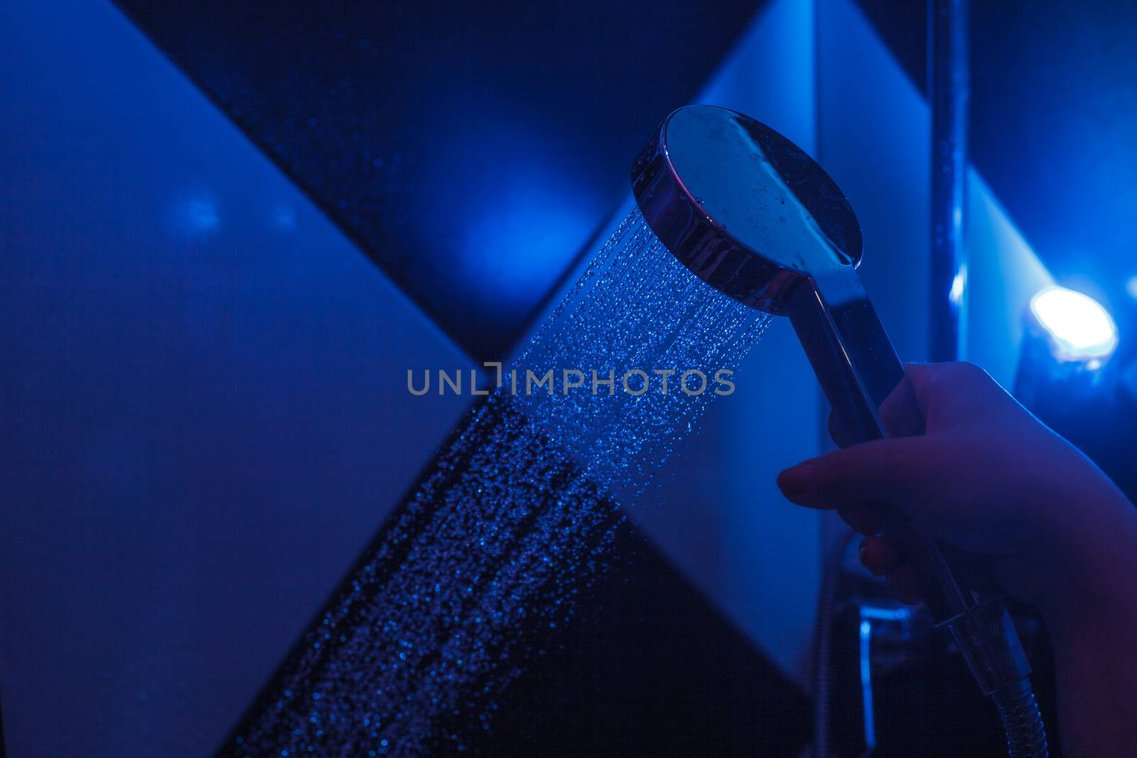 Girl holds a watering can in a shower cabin with blue backlight. Falling drops of water from a watering can.