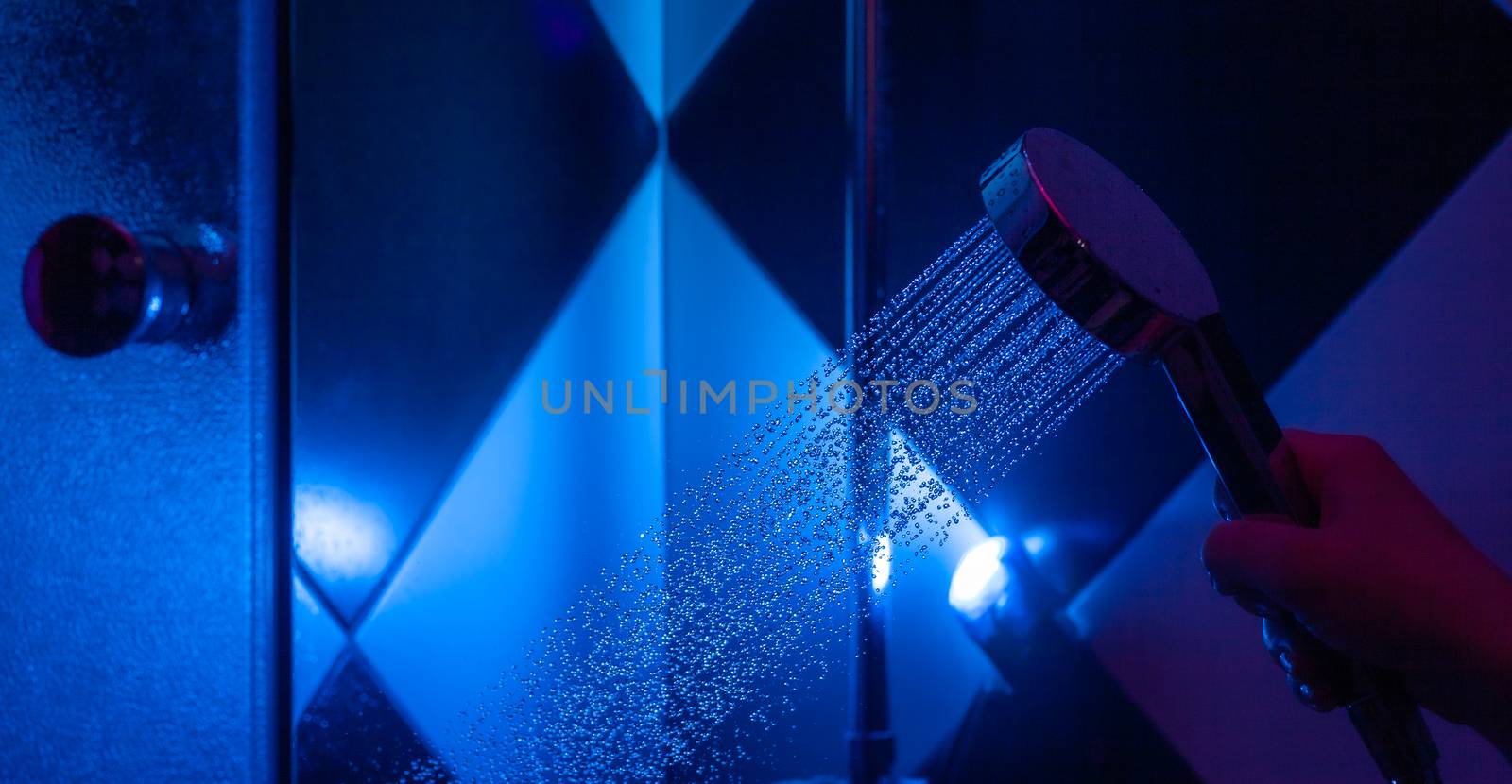 Girl holds a watering can in a shower cabin with blue backlight. Falling drops of water from a watering can.