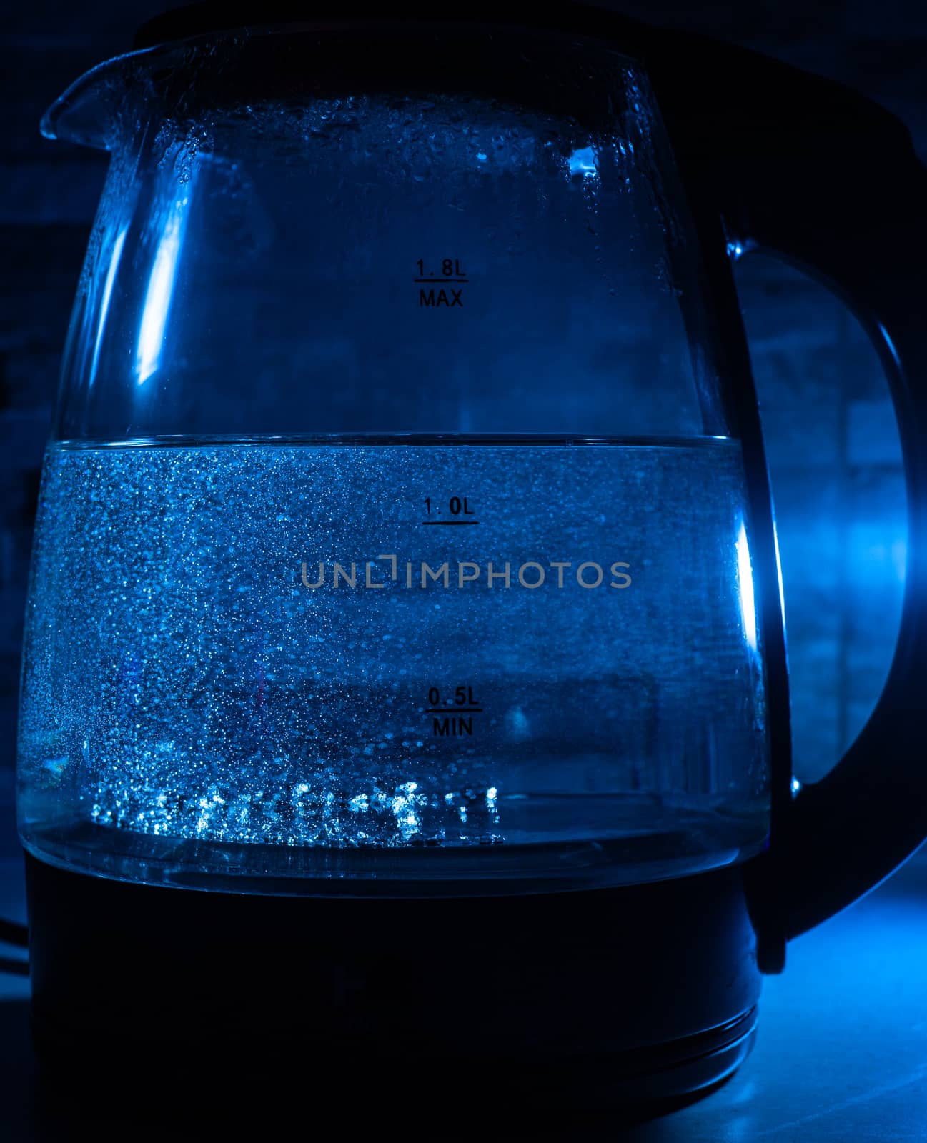 Boiling glass black teapot with blue backlight on a black background. Boiling water. Hot water is seething. Bubbles of air in the water.