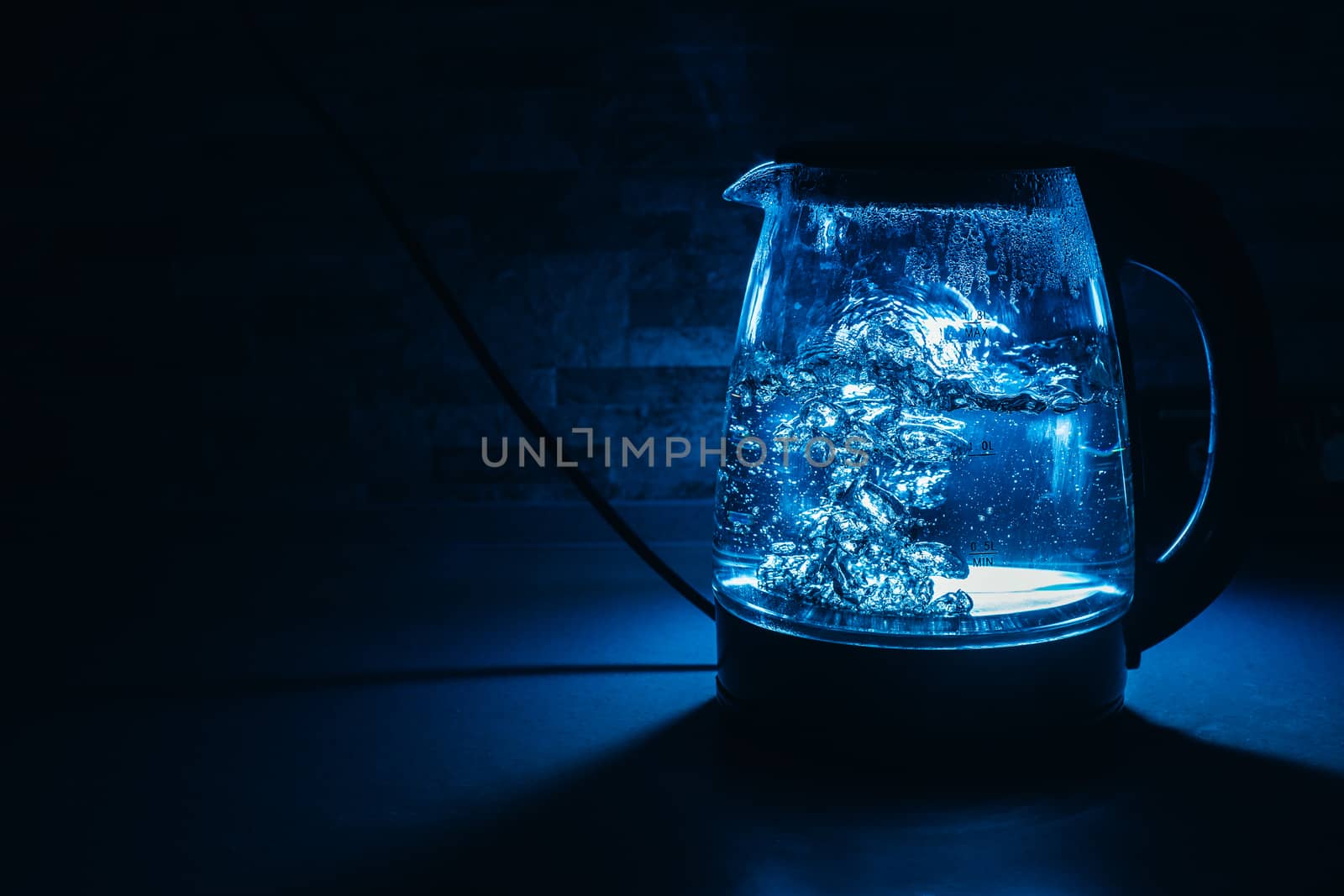 Boiling glass black teapot with blue backlight on a black background. Boiling water. Hot water is seething. Bubbles of air in the water.