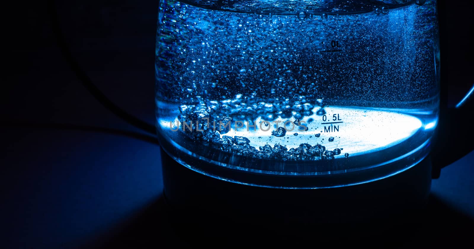 Boiling glass black teapot with blue backlight on a black background. Boiling water. Hot water is seething. Bubbles of air in the water.