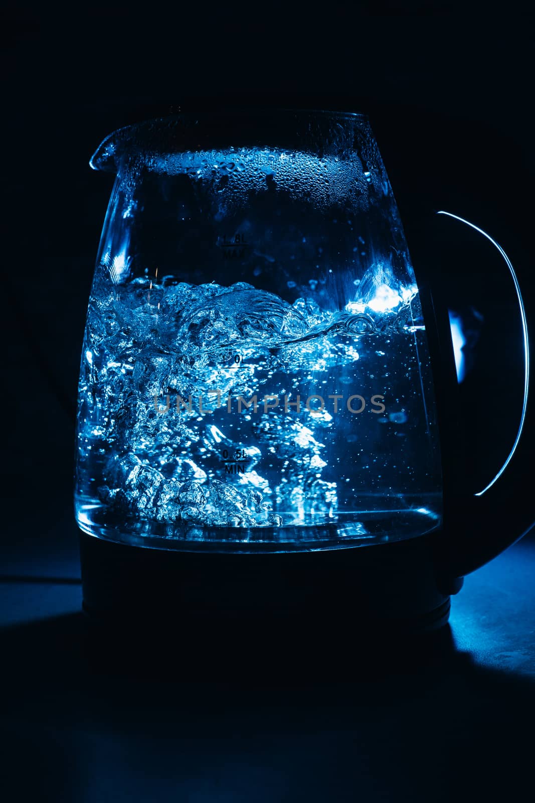 Boiling glass black teapot with blue backlight on a black background. Boiling water. Hot water is seething. Bubbles of air in the water.