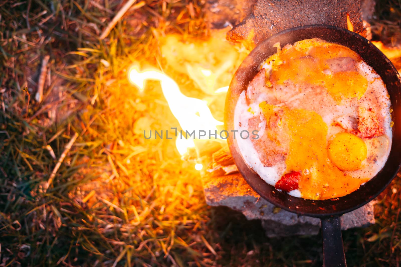 Fried eggs with bacon in a pan in the forest. Food at the camp. Scrambled eggs with bacon on fire. Lots of seasonings on fried eggs. Picnic