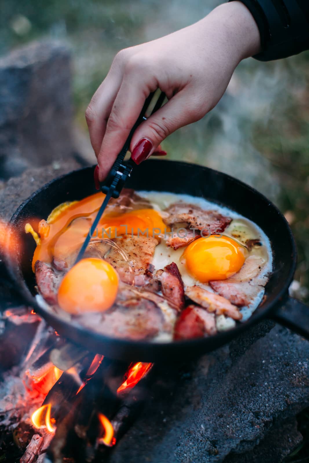Fried eggs with bacon in a pan in the forest. Food at the camp. Fried egg with bacon on fire. Рand with a knife in a pan . Picnic